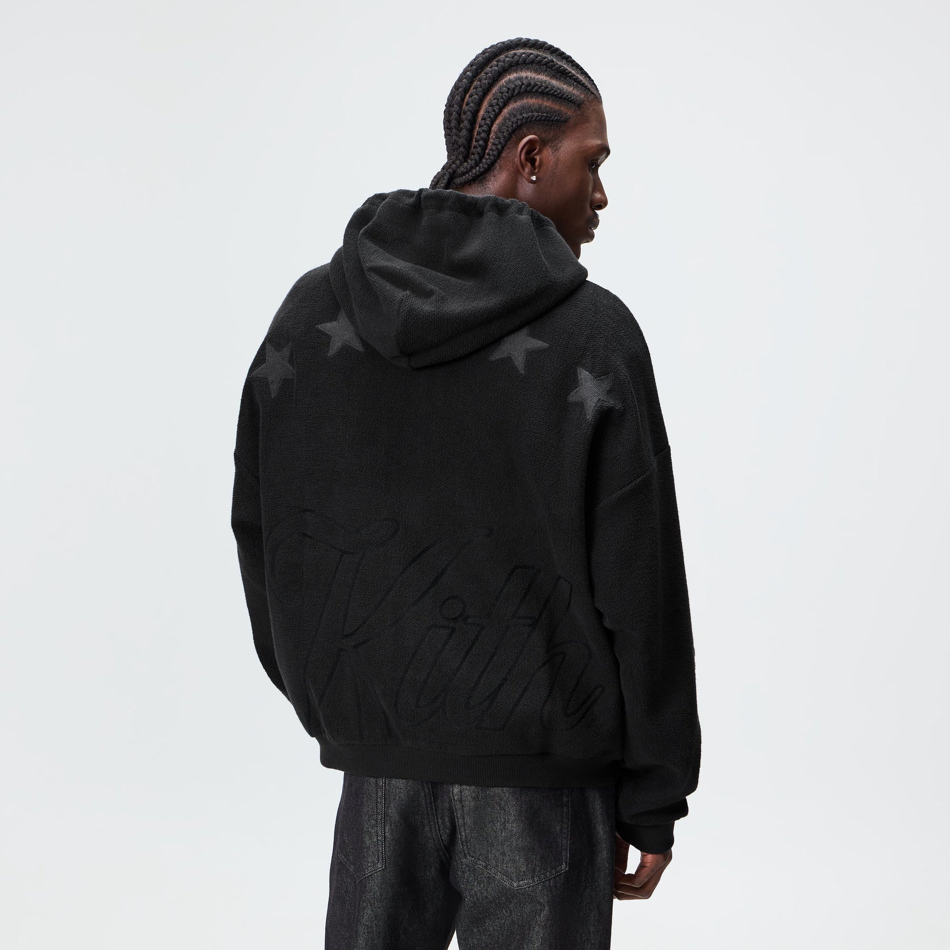 Man wearing the Kith Varsity Braxton hoodie in black, back view showing tonal star and script graphics