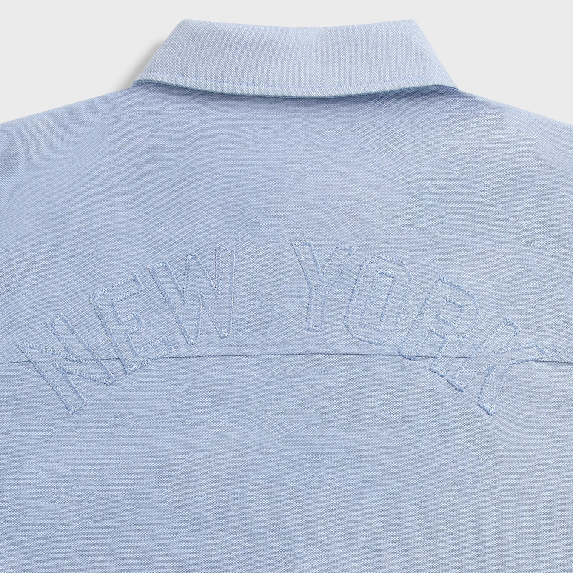 Close-up of New York embroidered lettering on the back yoke of light blue Oxford Deon overshirt