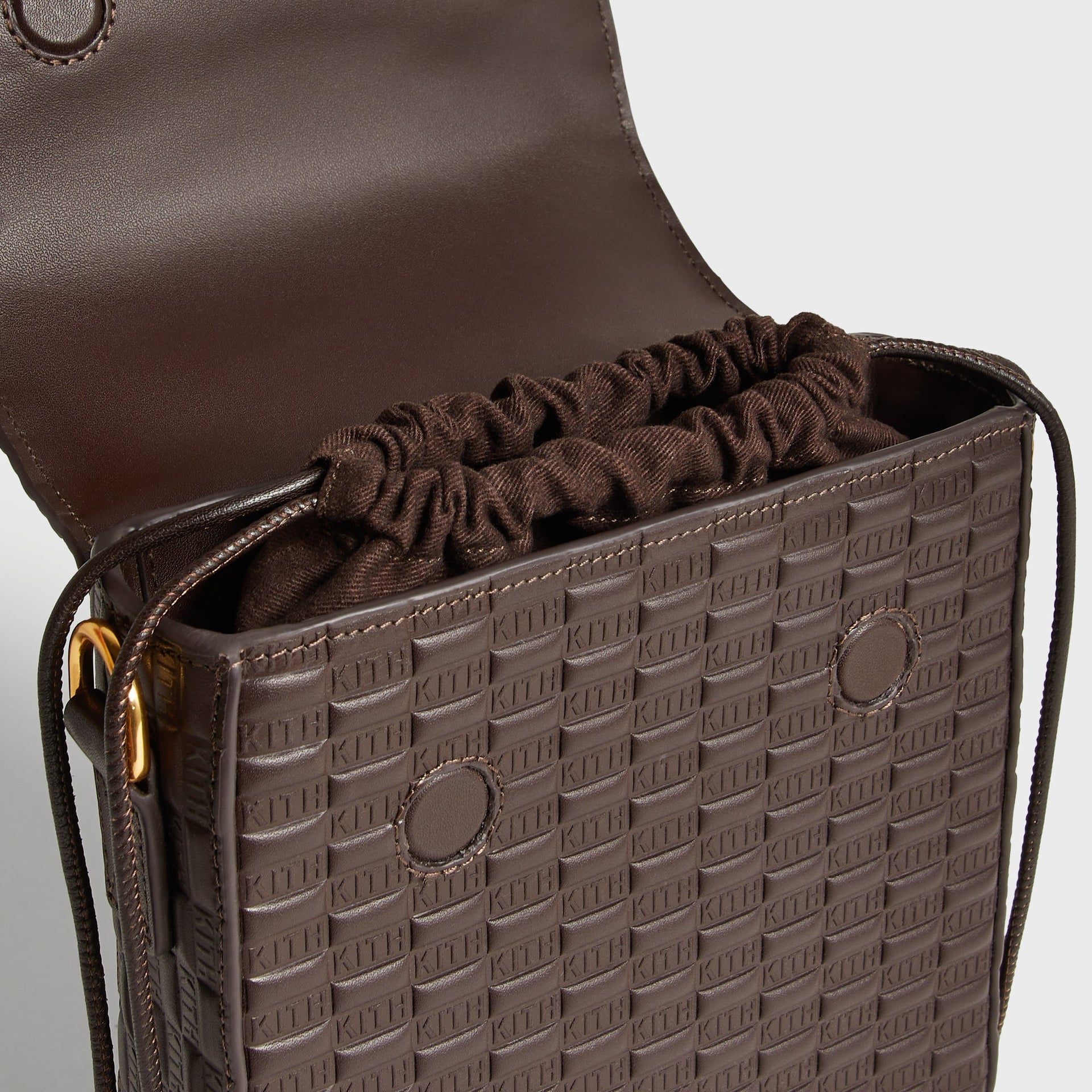 Interior view of the Kith Monogram Smooth Leather Explorer Pack with flap open, revealing the drawstring fabric pouch closure and embossed leather lining