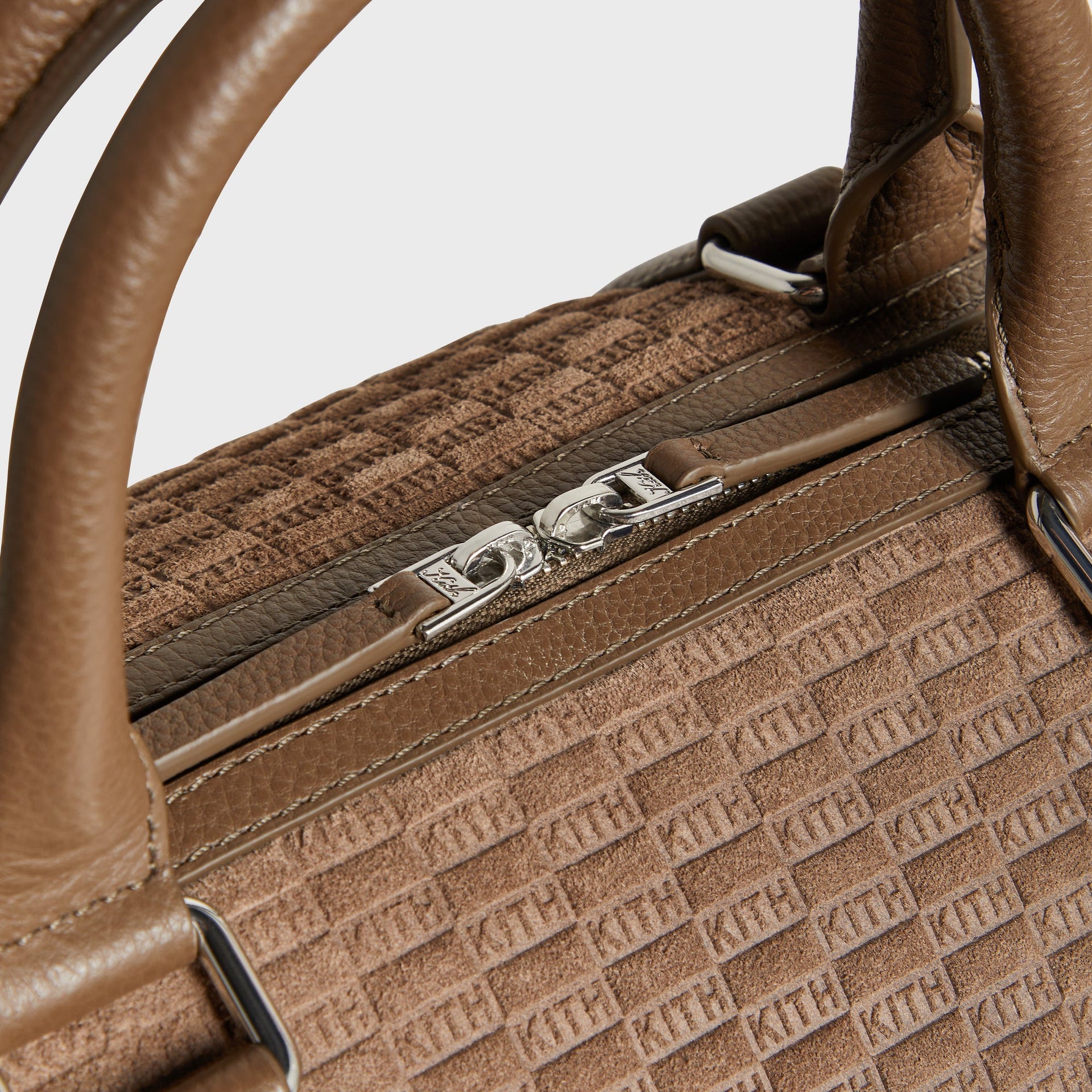 Close-up detail of top zipper pulls and handle hardware on the Kith Monogram Suede Traveler Duffle Bag