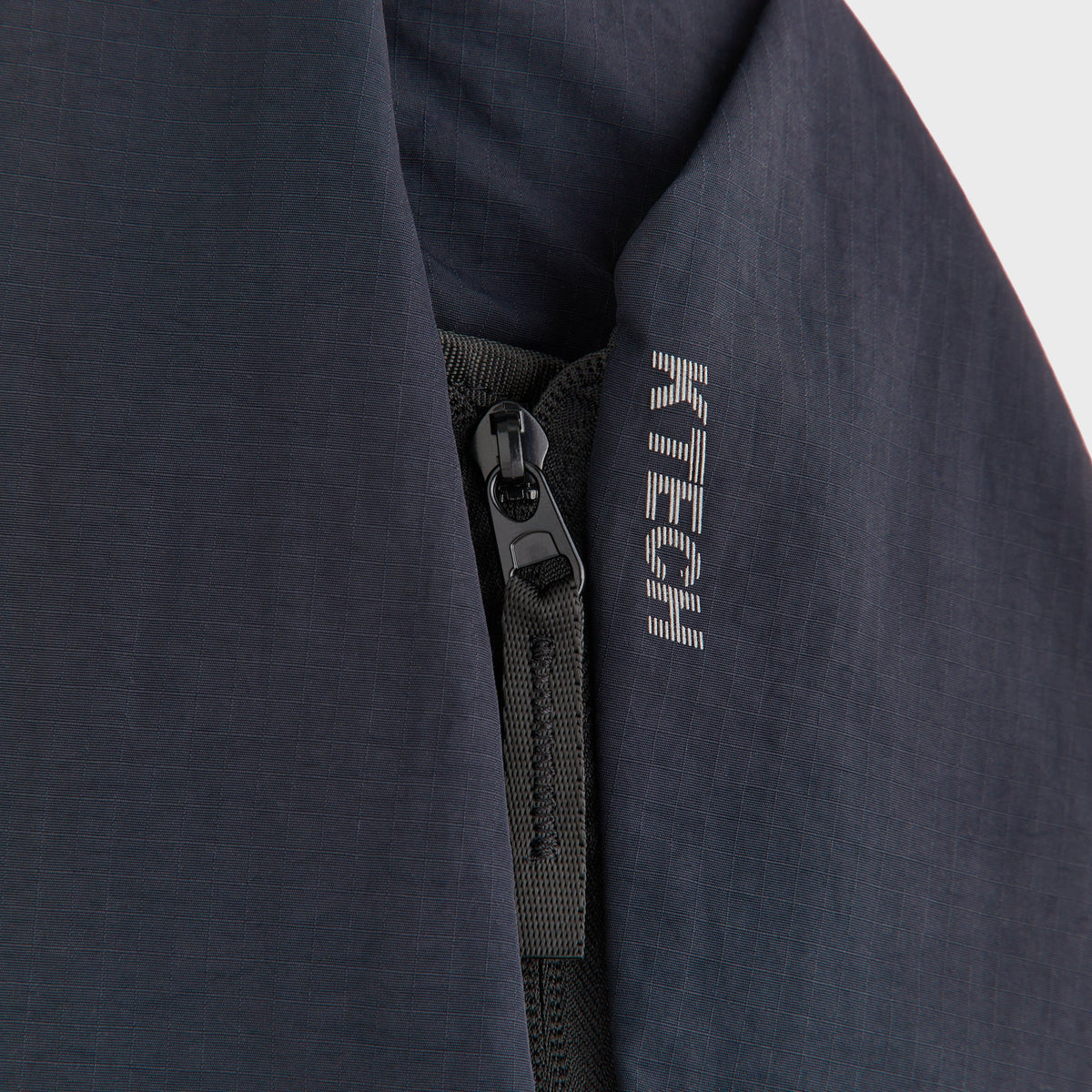 Close-up of the front zip pocket and dual zipper pulls on the Kith ripstop sling backpack