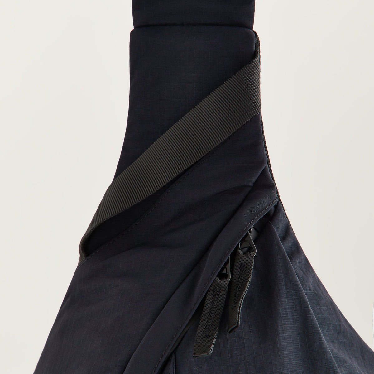 Close-up of a zippered compartment and pull tabs on the Kith Nylon Ripstop Sling Backpack