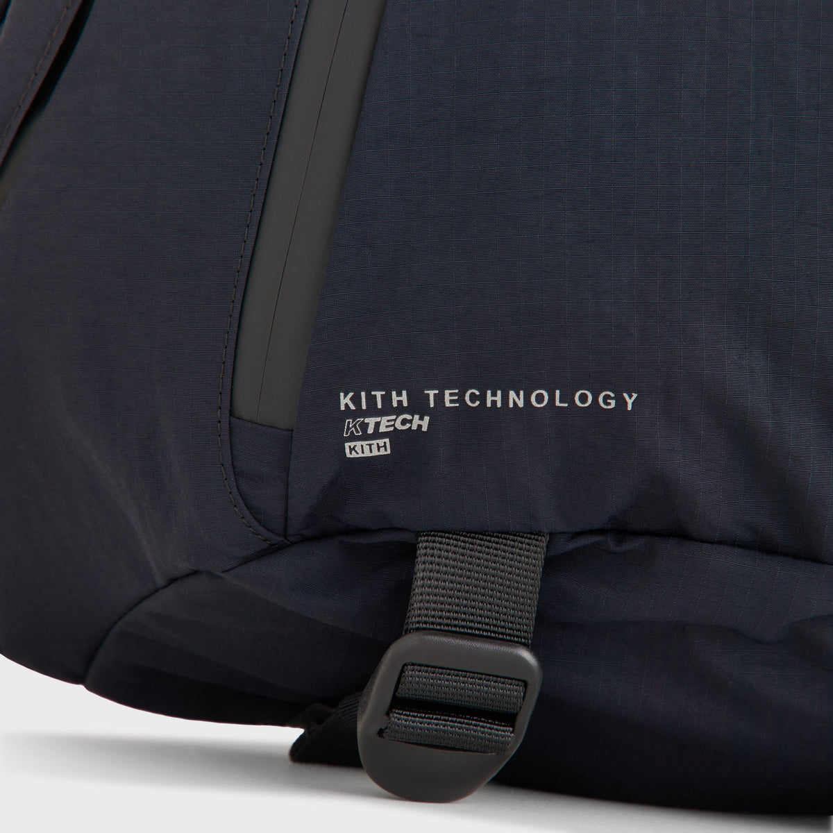 Close-up of the Kith Technology KTECH print on the ripstop nylon fabric of the sling backpack