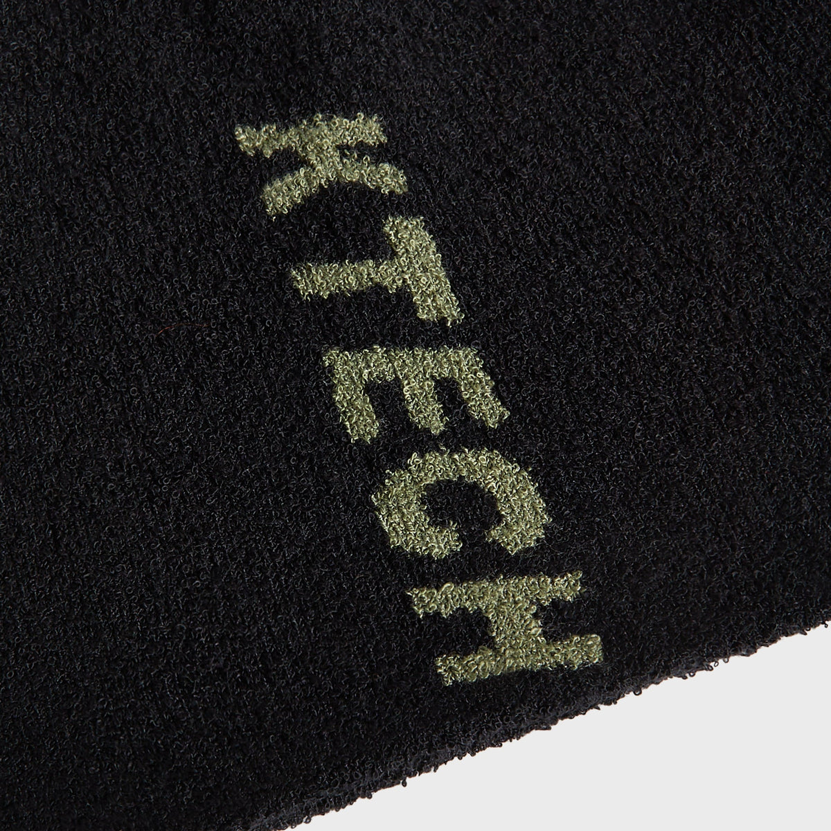 Macro close-up of the green KTECH logo knit into the black bouclé fabric of the Kith beanie