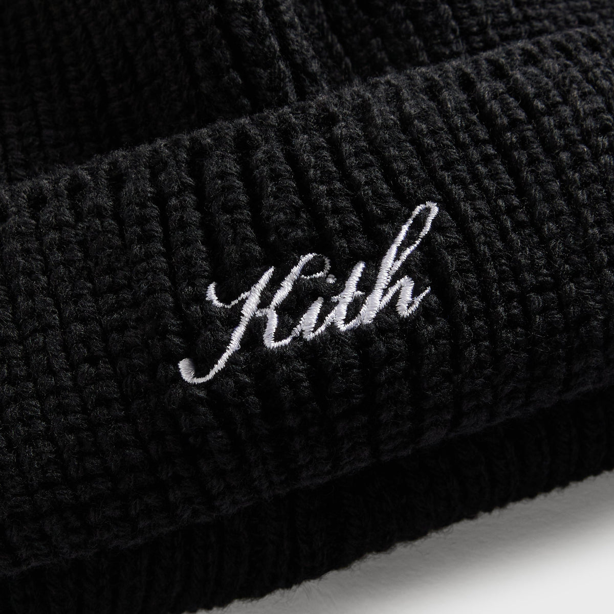 Close-up of white Kith script embroidery on black ribbed knit shallow beanie cuff