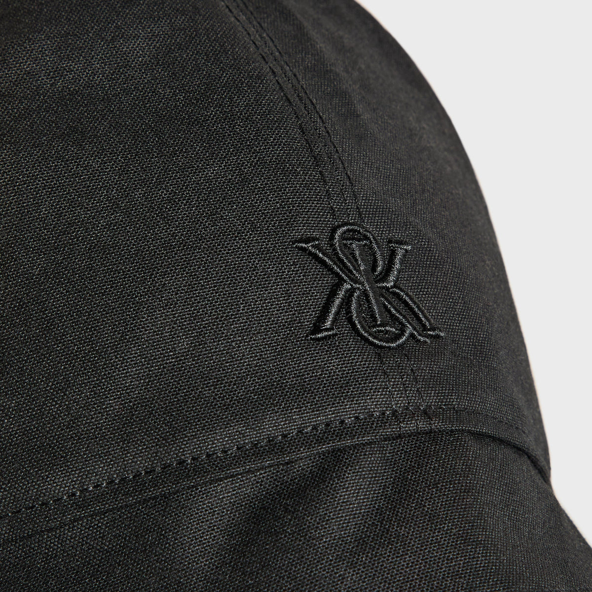 Close-up of black embroidered Kith & Kin logo on black waxed canvas trapper hat
