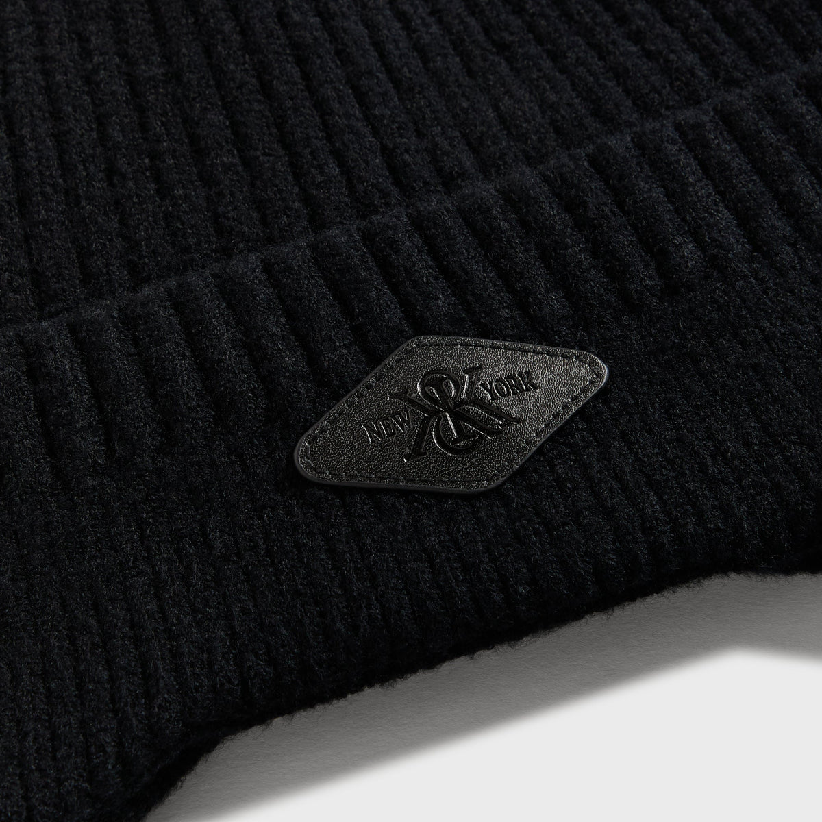 Close-up of black diamond leather Kith patch on black chunky knit earflap beanie