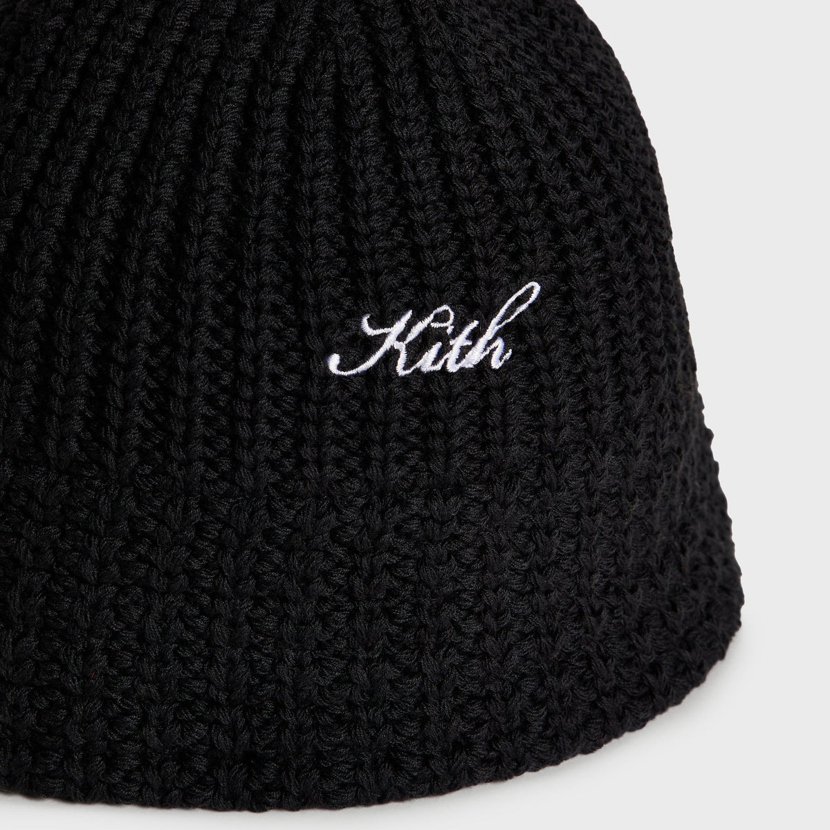 Close-up of white Kith script embroidery on black chunky knit bucket hat