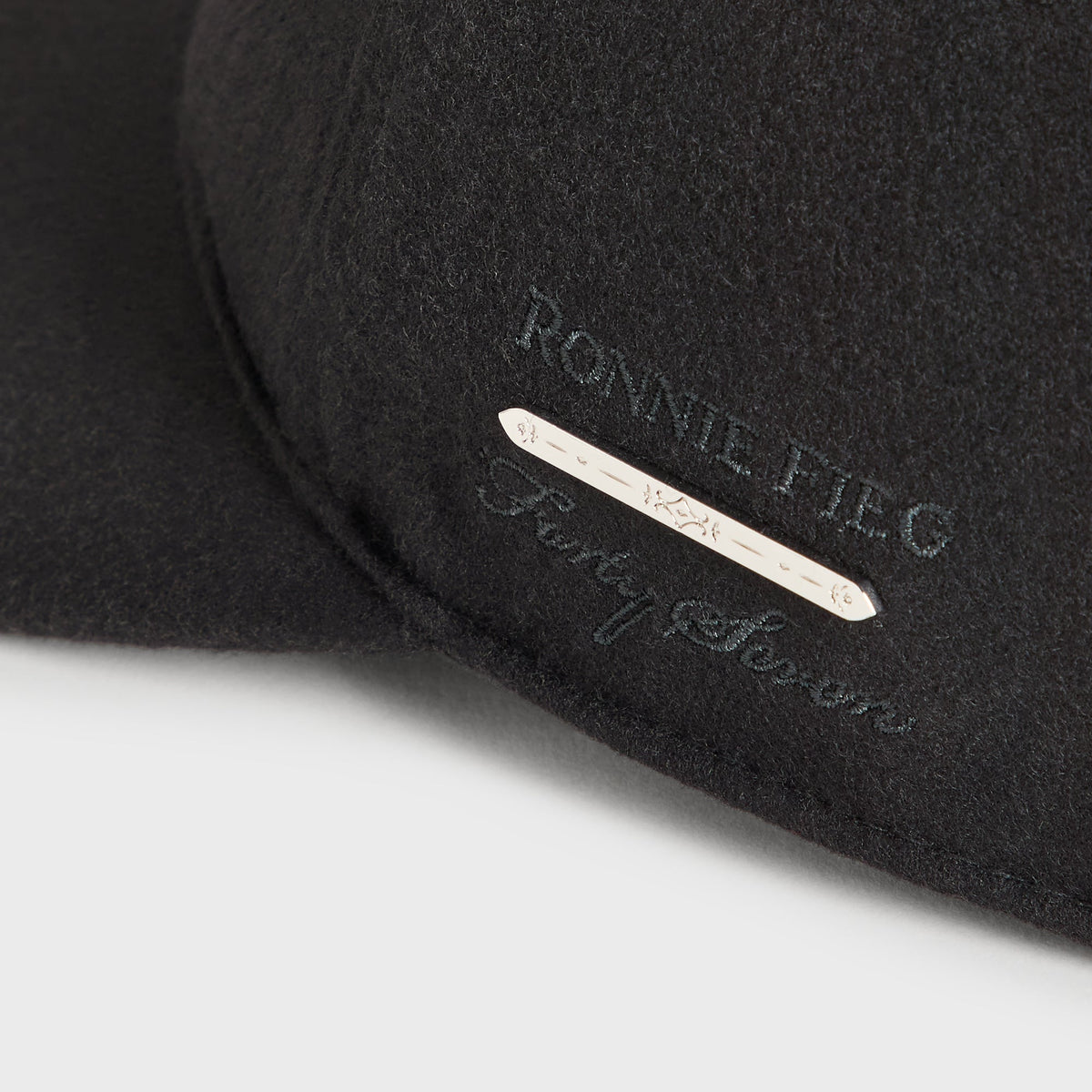 Close-up of Ronnie Fieg for Forty Seven metal bar tag and debossed lettering on the Giorgio Armani black wool fitted cap