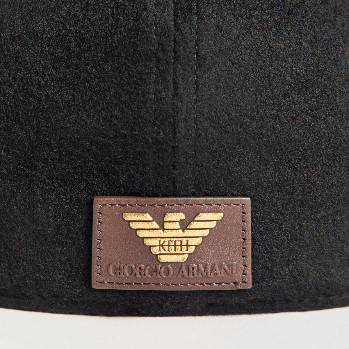 Close-up of brown leather Kith Giorgio Armani gold eagle patch on the back of the black wool fitted cap