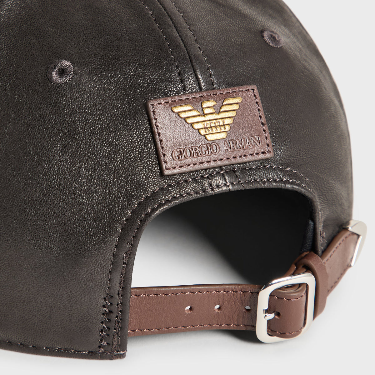 Close-up of brown leather strap with silver buckle and Armani eagle patch on the black soft leather Hitch cap