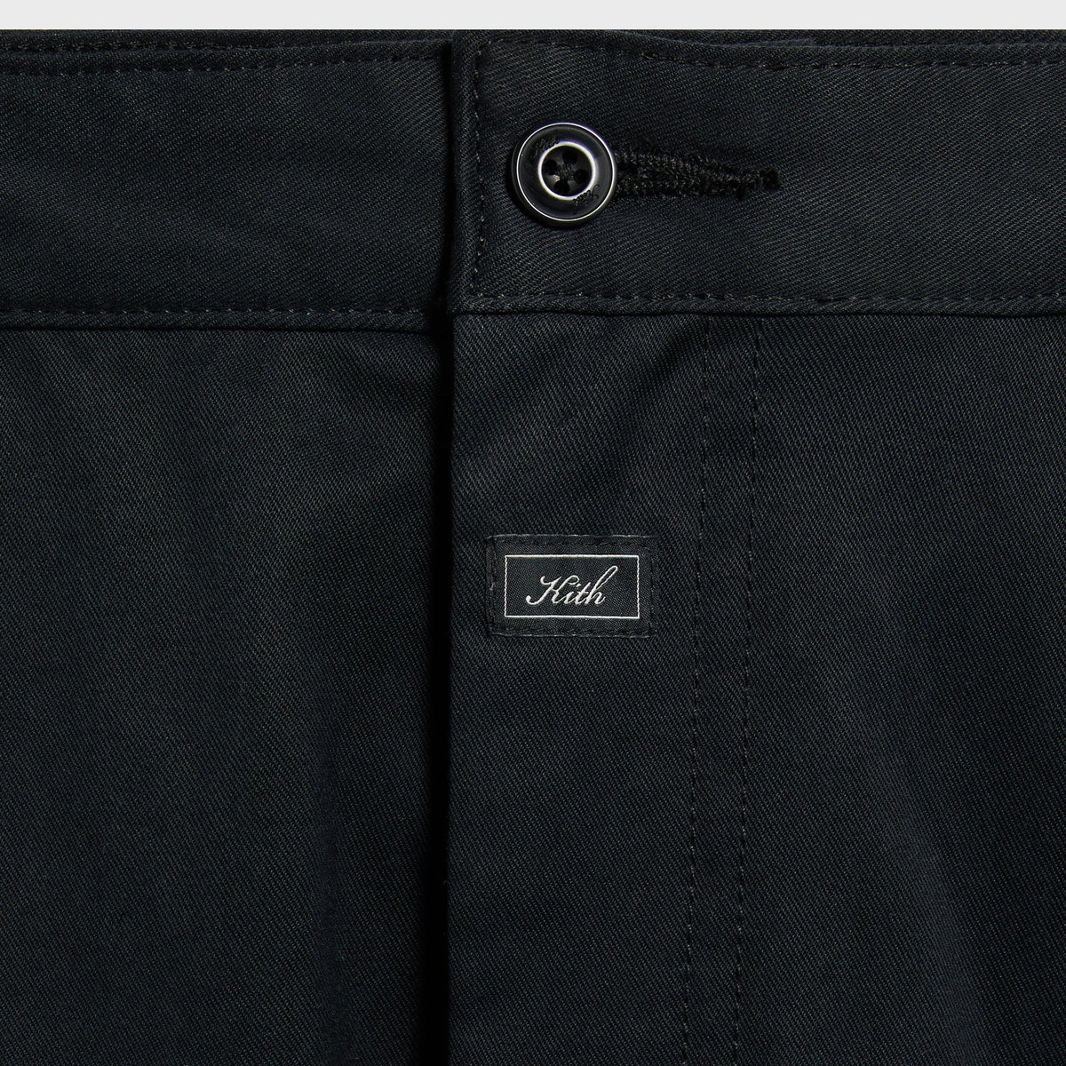 Kith Washed Herringbone Twill Gus Pant in black, close-up of waistband button, fly and woven Kith script label