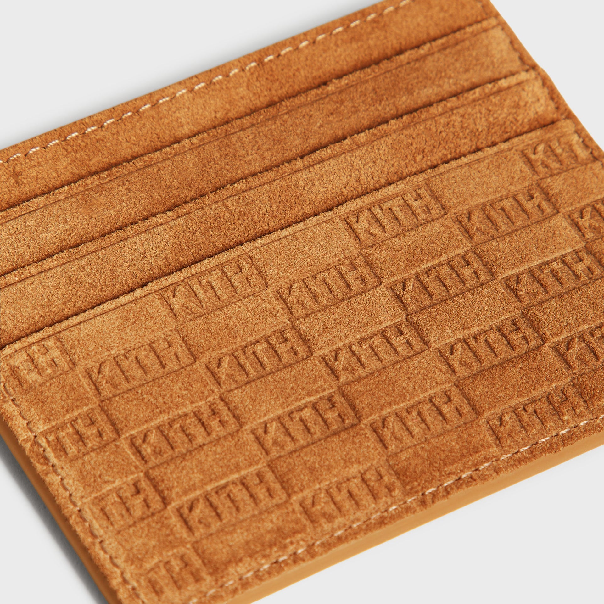 Close-up of the suede exterior stitching and embossed KITH monogram pattern on the cardholder edge