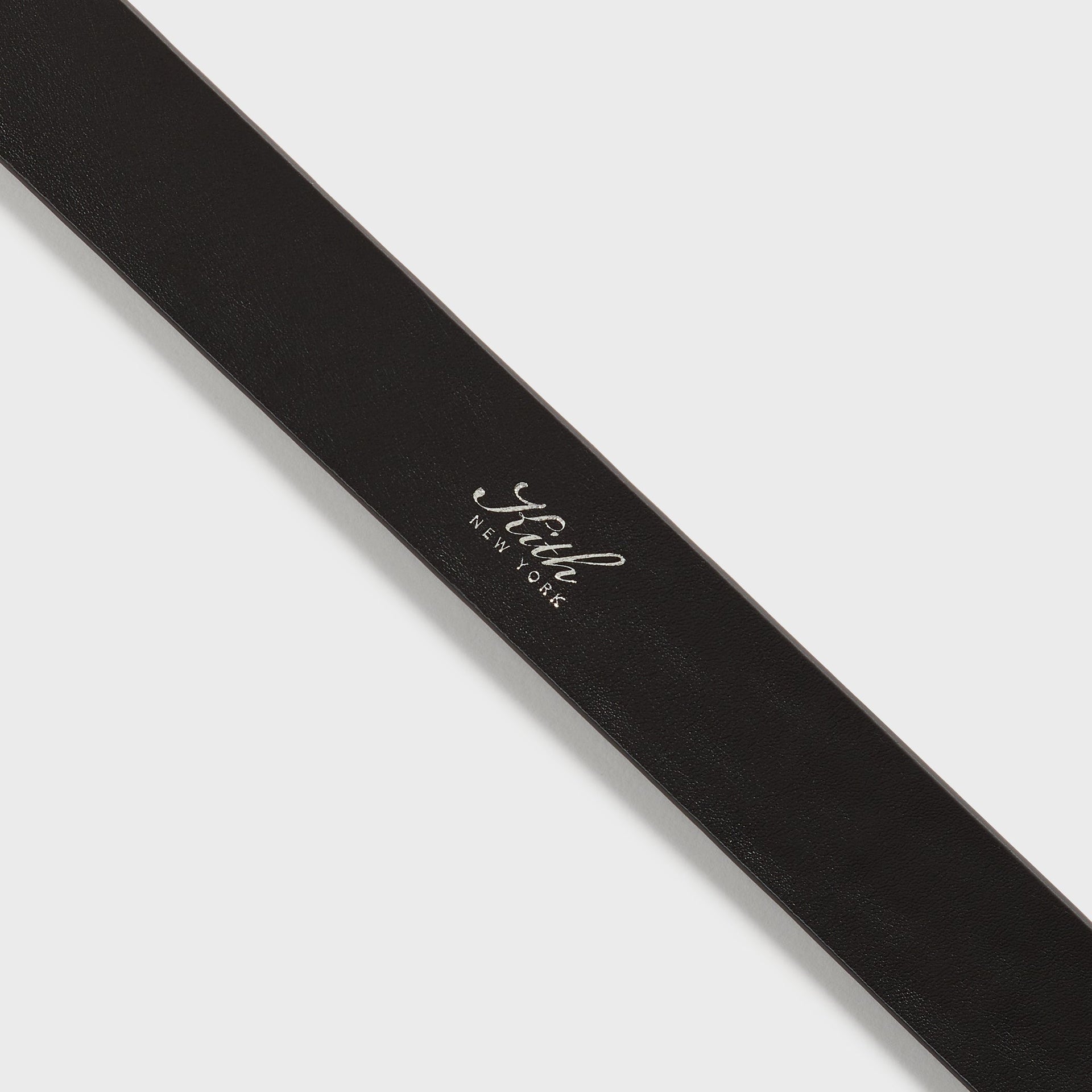 Kith Monogram Tumbled Leather Belt in Black, close-up of Kith New York foil logo print on smooth leather strap