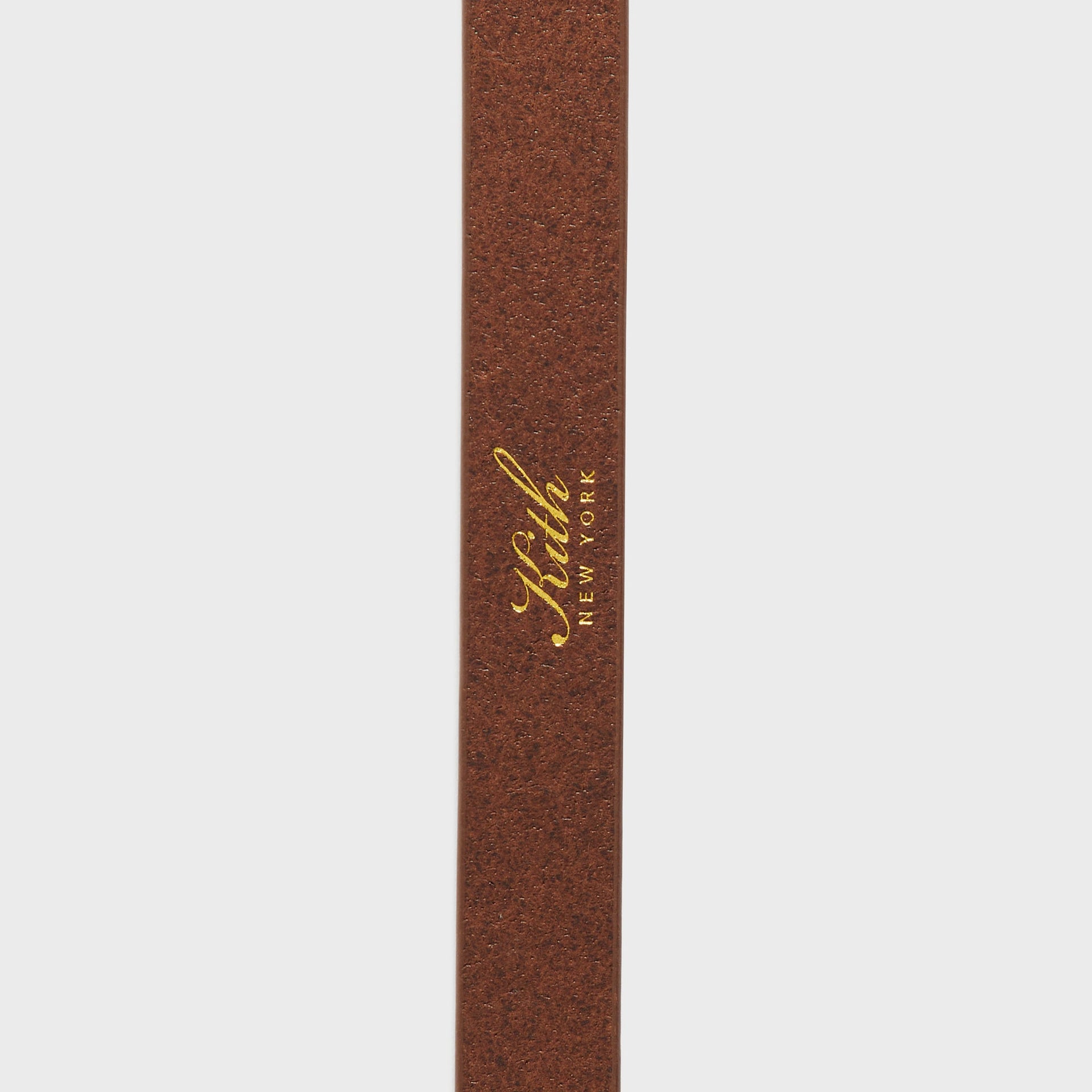 Vertical detail of cognac leather strap on Kith Western Smooth Leather Belt with gold foil-stamped Kith New York logo