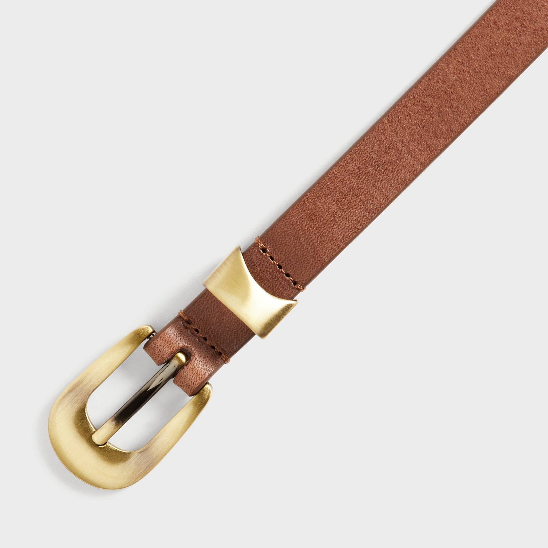 Close-up angled view of the brass horseshoe buckle and keeper on the Kith Western Smooth Leather Belt