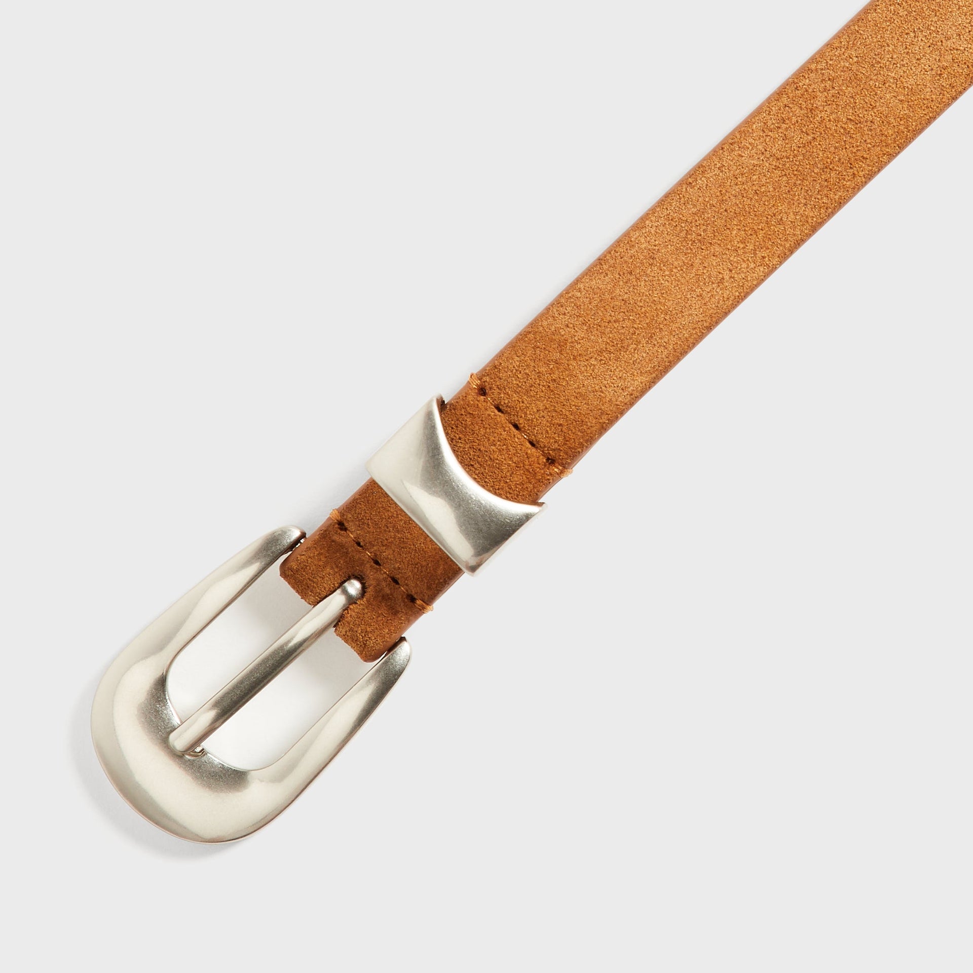 Close-up of the Kith Western Suede Belt in Argil buckle hardware, showing the silver western buckle and keeper loop on tan suede