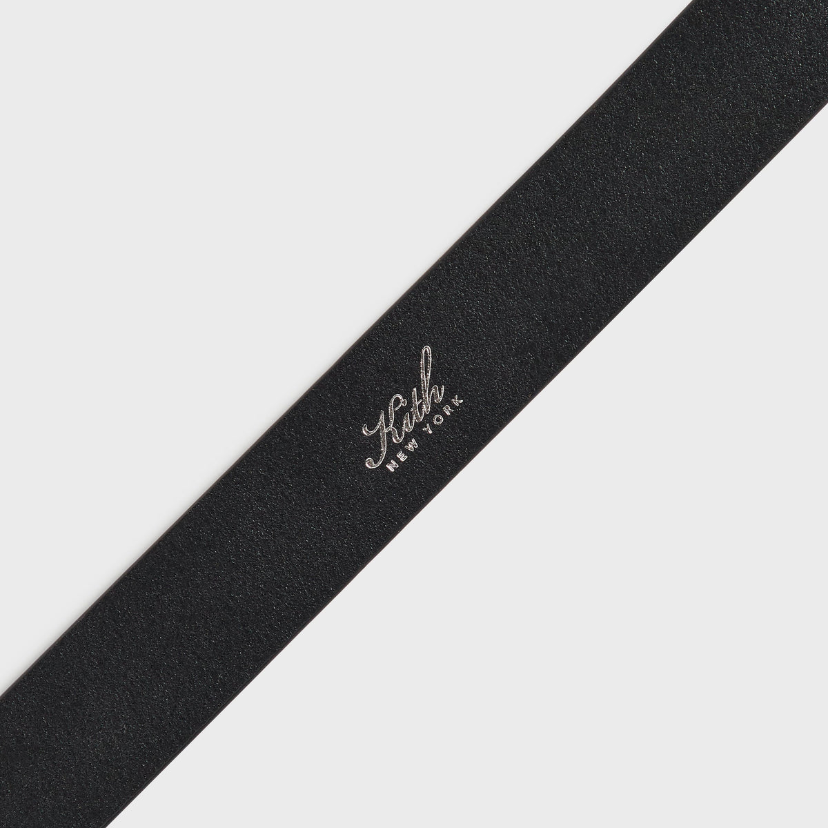 Close-up of Kith New York script logo stamped on black leather belt strap