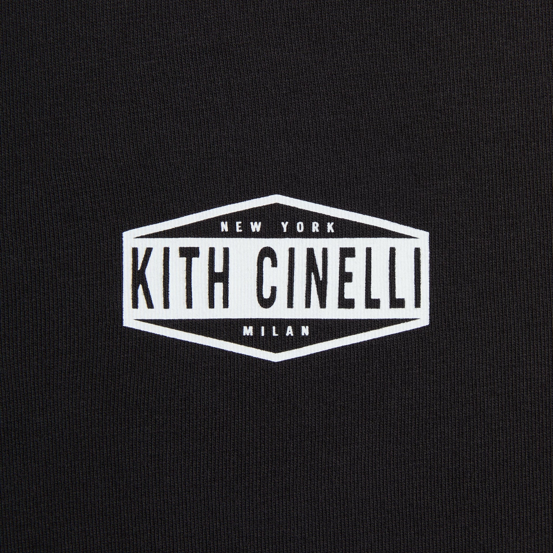 Close-up of the white hexagonal Kith Cinelli New York Milan chest badge printed on black jersey