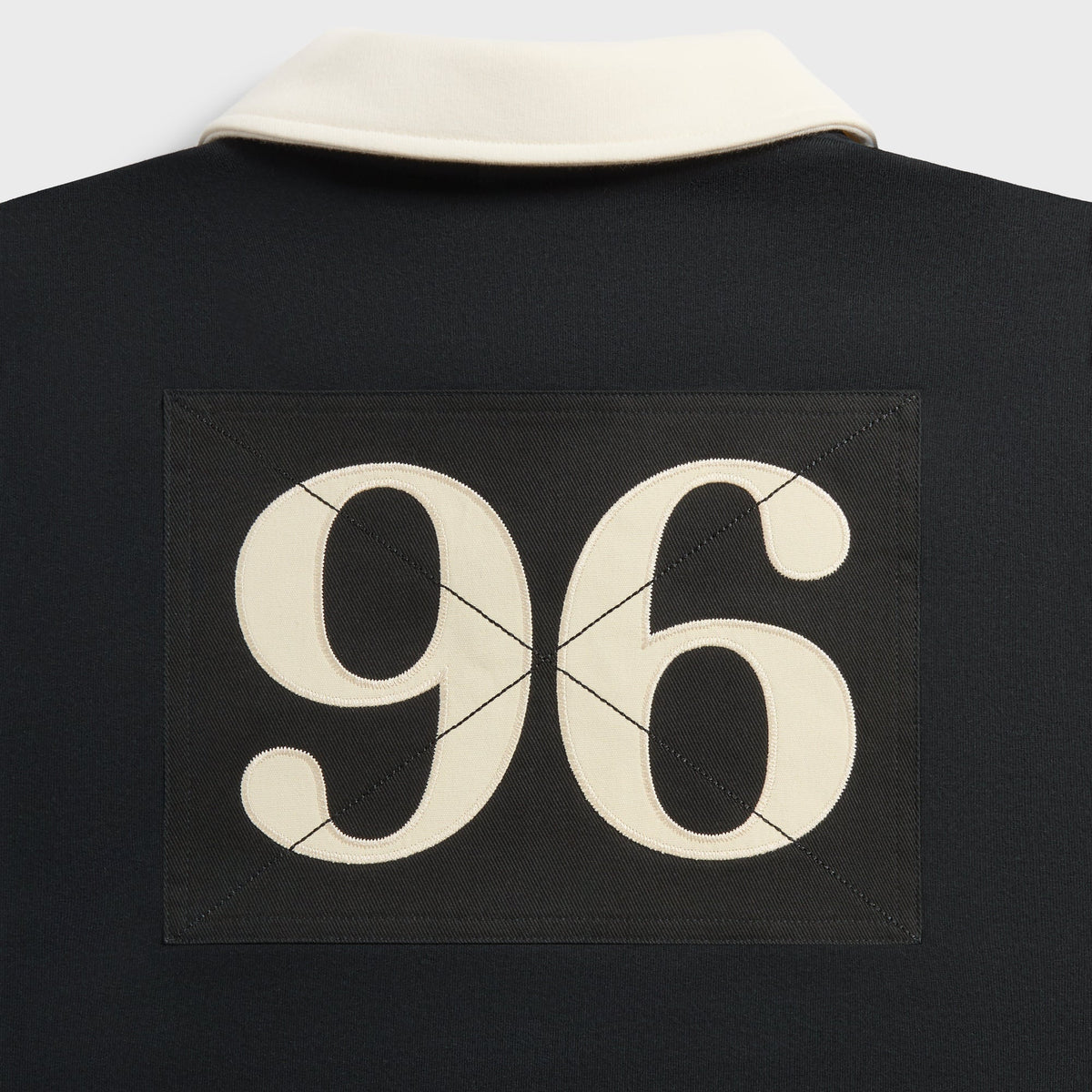 Close-up of cream 96 appliqué on black back panel below the cream collar of the Kith Vancouver Nelson rugby