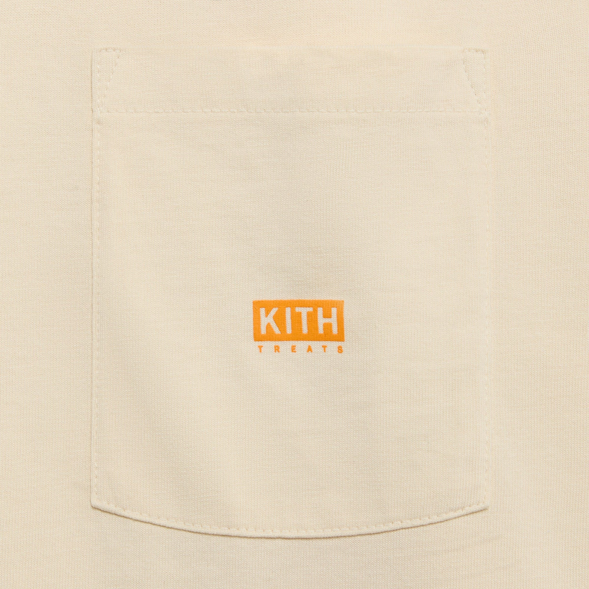 Close-up of Kith Treats Pumpkin Harvest Pocket Tee chest pocket with orange Kith Treats logo patch on cream cotton
