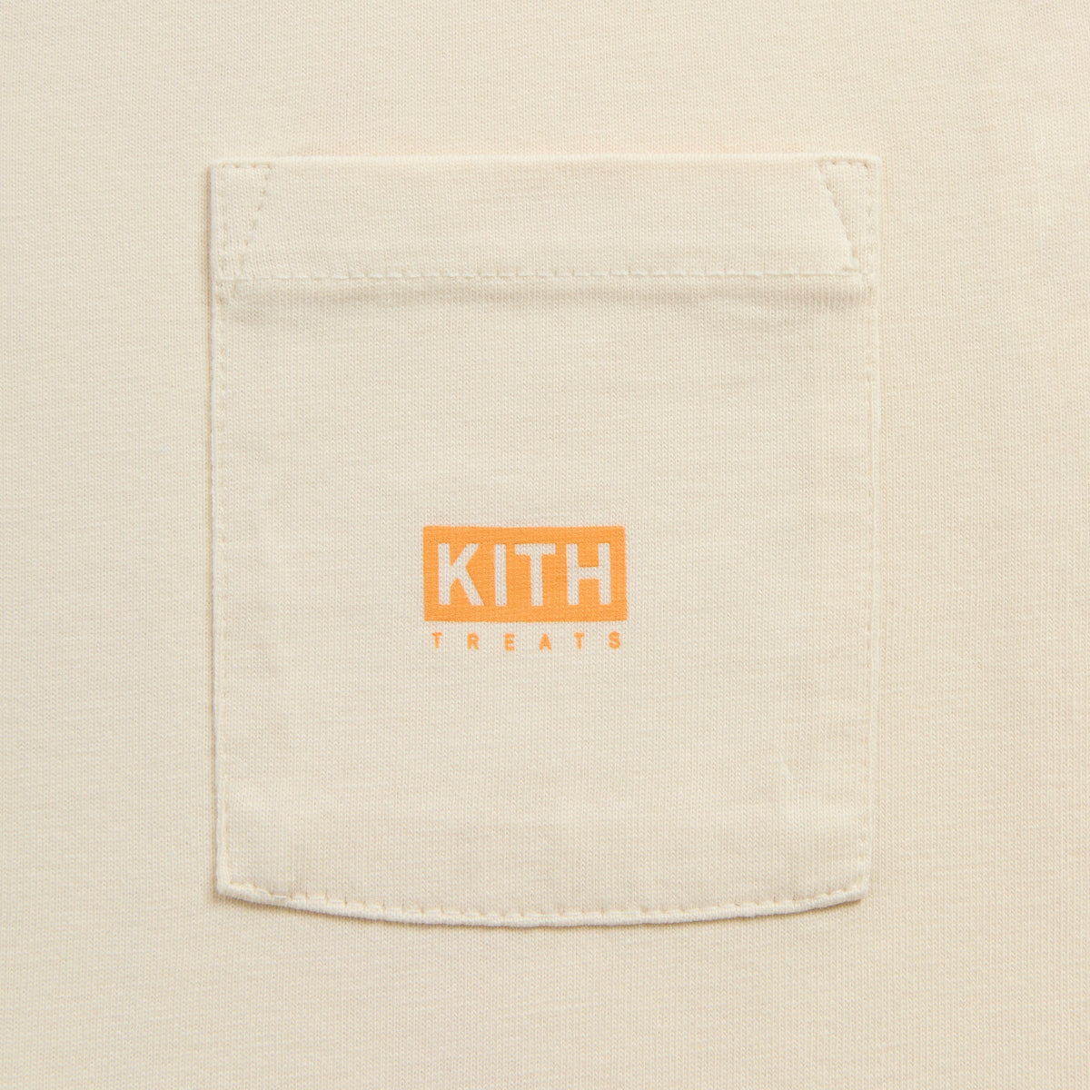 Close-up of Kith Kids Pumpkin Harvest Pocket Tee chest pocket with orange Kith Treats logo patch on cream cotton