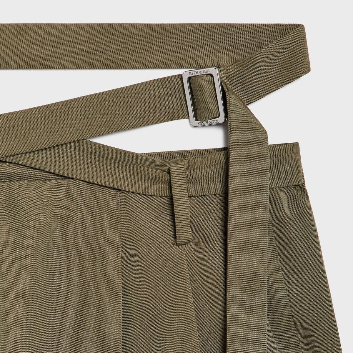 Close-up of the Kith & Kin engraved buckle on the waist strap of the Tallis trouser in Chelonian olive