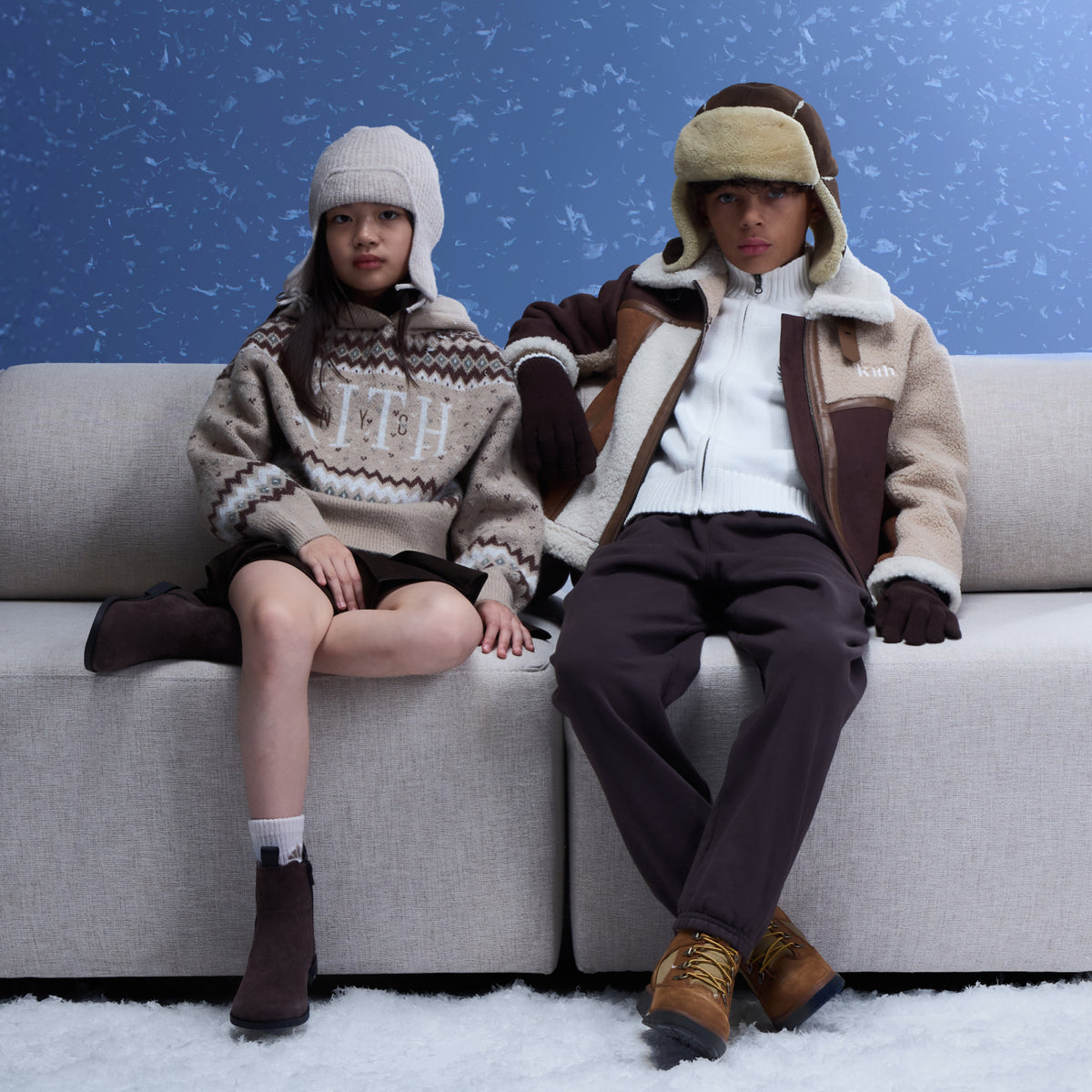 Two children on a sofa in a Kith Fair Isle sweater and shearling aviator jacket with a trapper hat, snowy scene