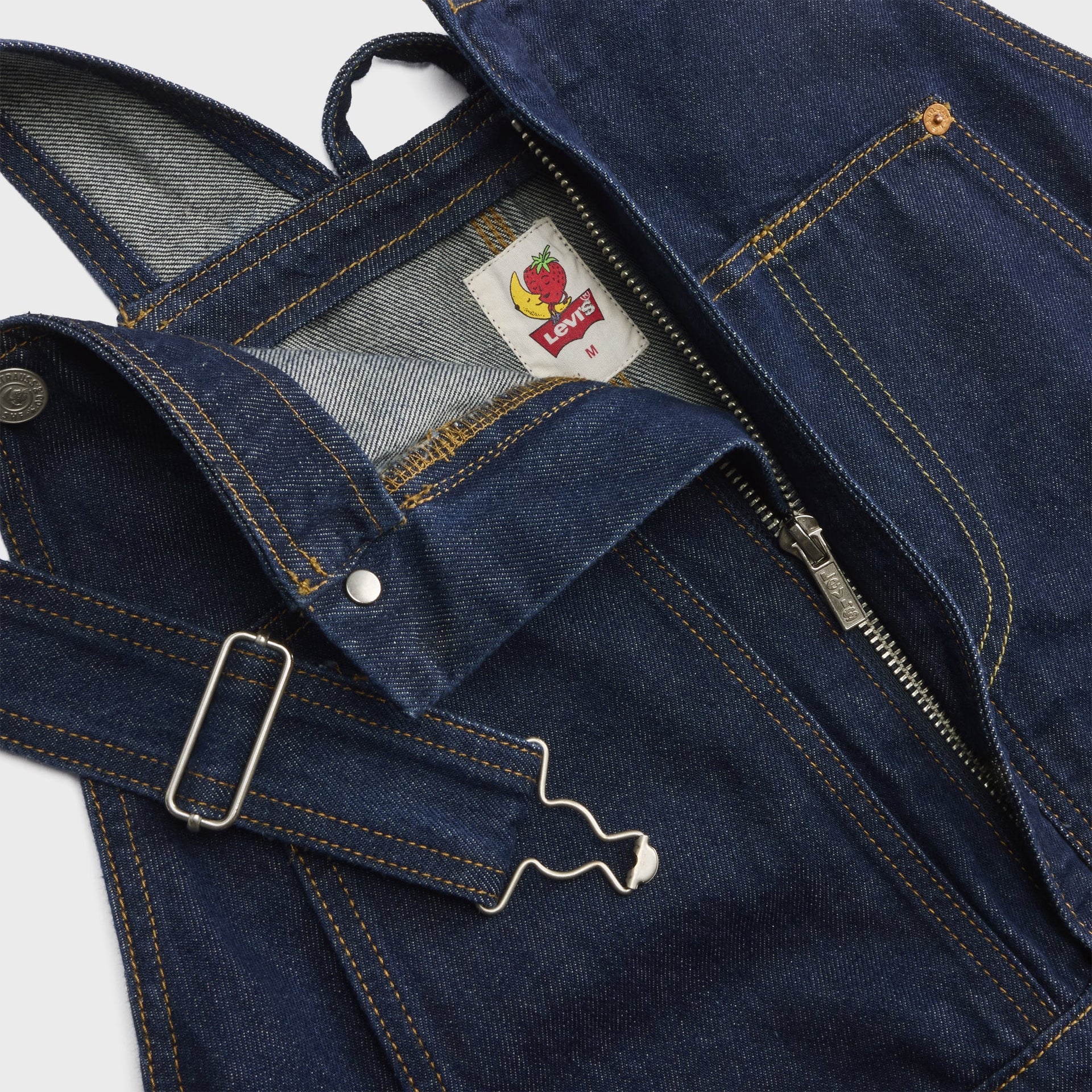 Detail of Levi's x Sky High Farm overalls bib with side zip, silver strap buckle and woven banana-and-strawberry Levi's label