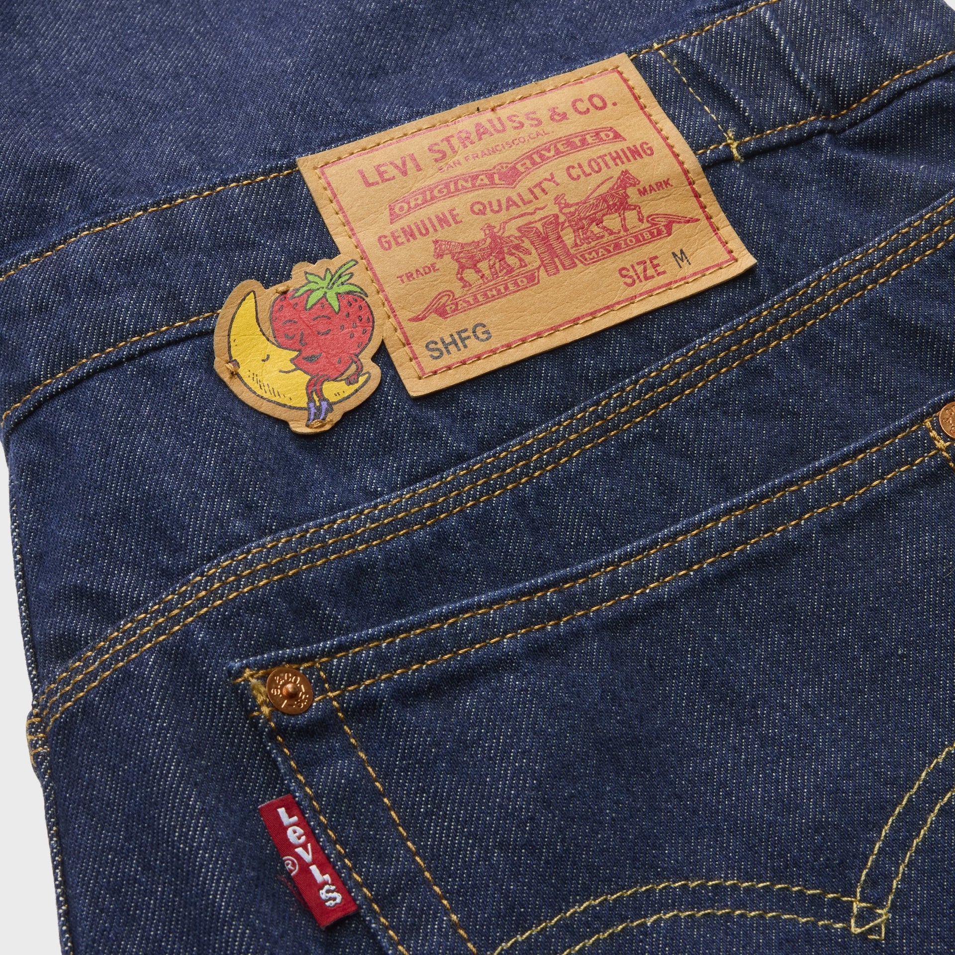 Detail of Levi's x Sky High Farm overalls back waist with leather 'SHFG' patch, banana-and-strawberry decal and red Levi's tab