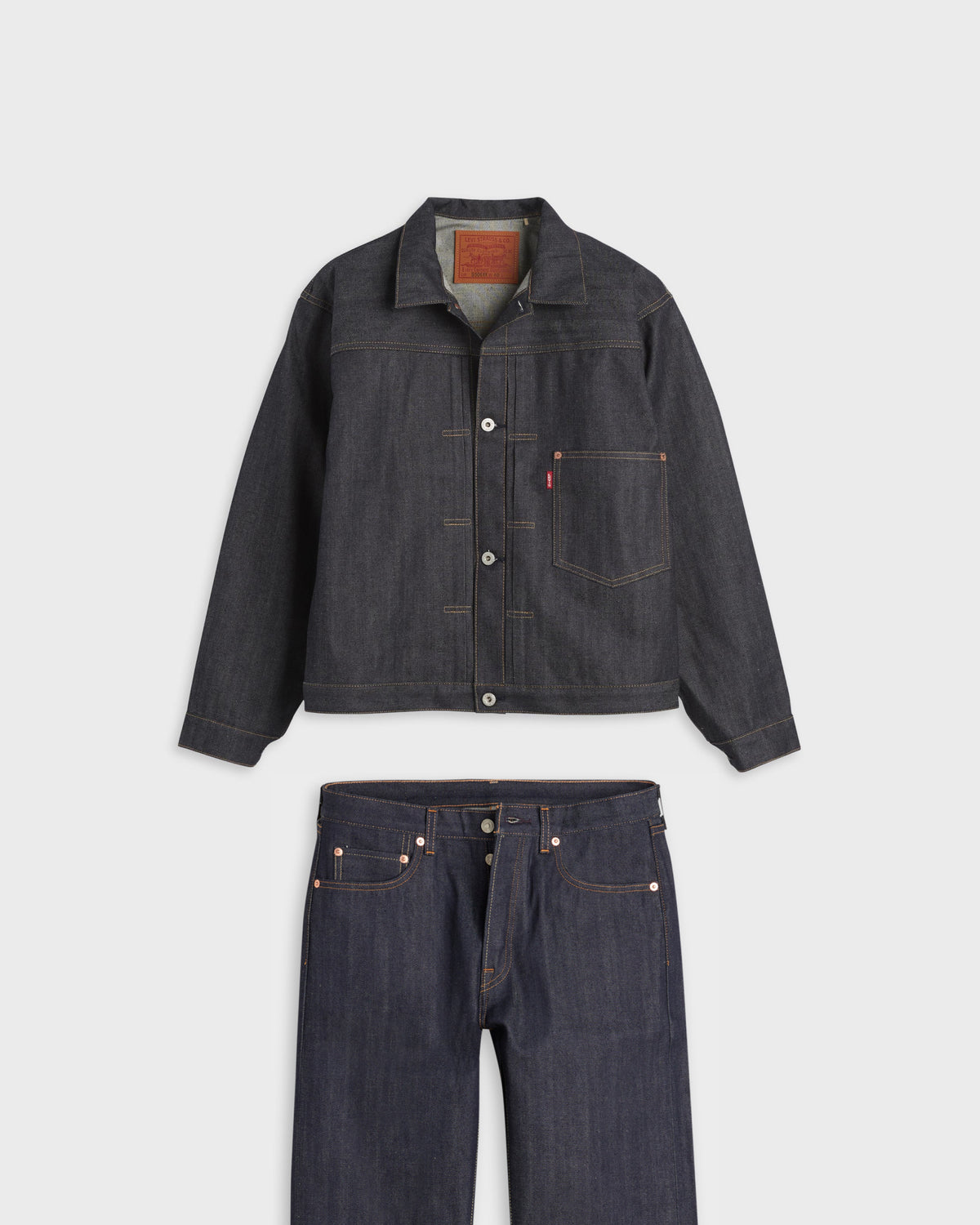 Levi's dark indigo denim trucker jacket with matching raw denim jeans, flat lay on light gray