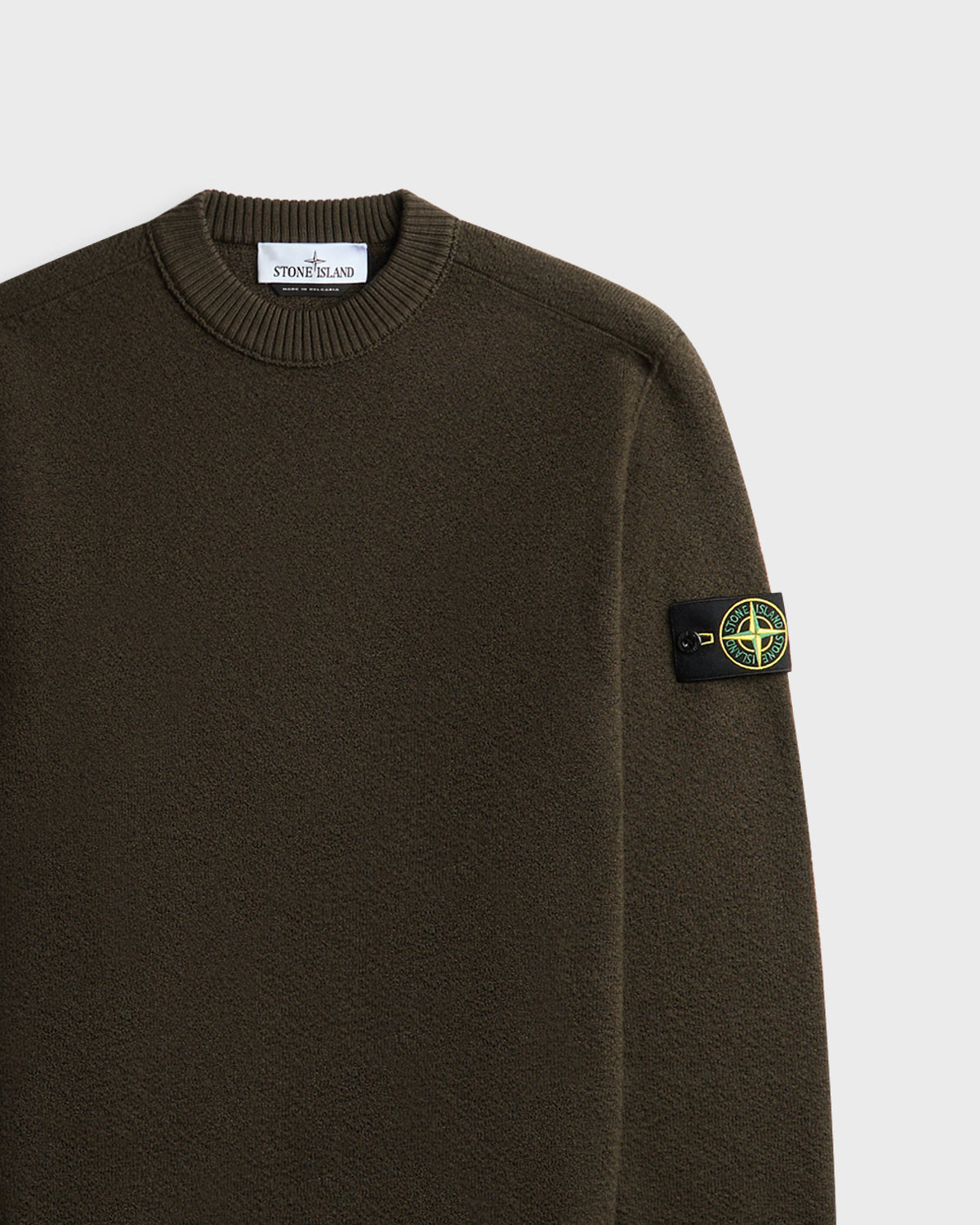 Close-up of olive green Stone Island crewneck sweater with logo patch on sleeve and woven collar label