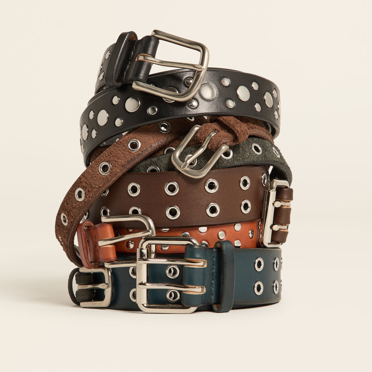 Stack of five studded and grommet leather belts in black, brown, orange, green and navy with silver buckles
