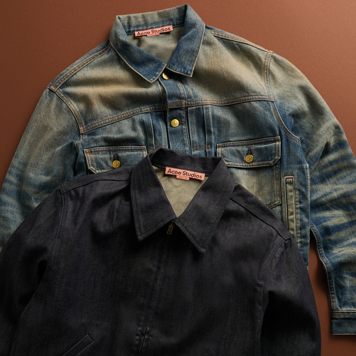 Two Acne Studios denim jackets, light wash and dark indigo, layered flat with pink logo neck tags visible