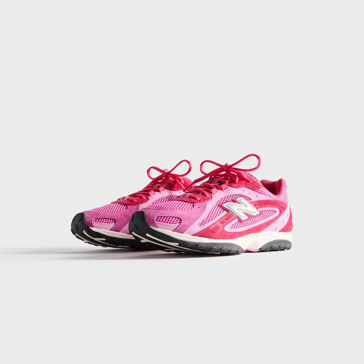Kith & New Balance 204L in Camellia, front three-quarter view of the pink and red pair with mesh toe and silver N logos