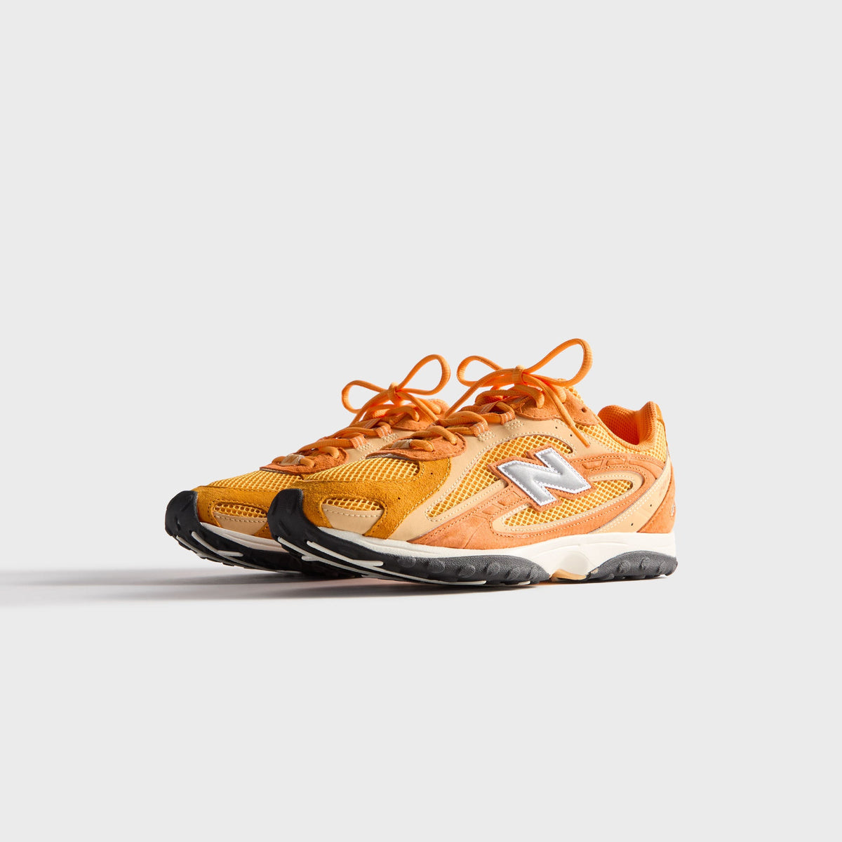 Kith & New Balance 204L in Sunburst, front three-quarter view of the orange pair with mesh toe and silver N logos