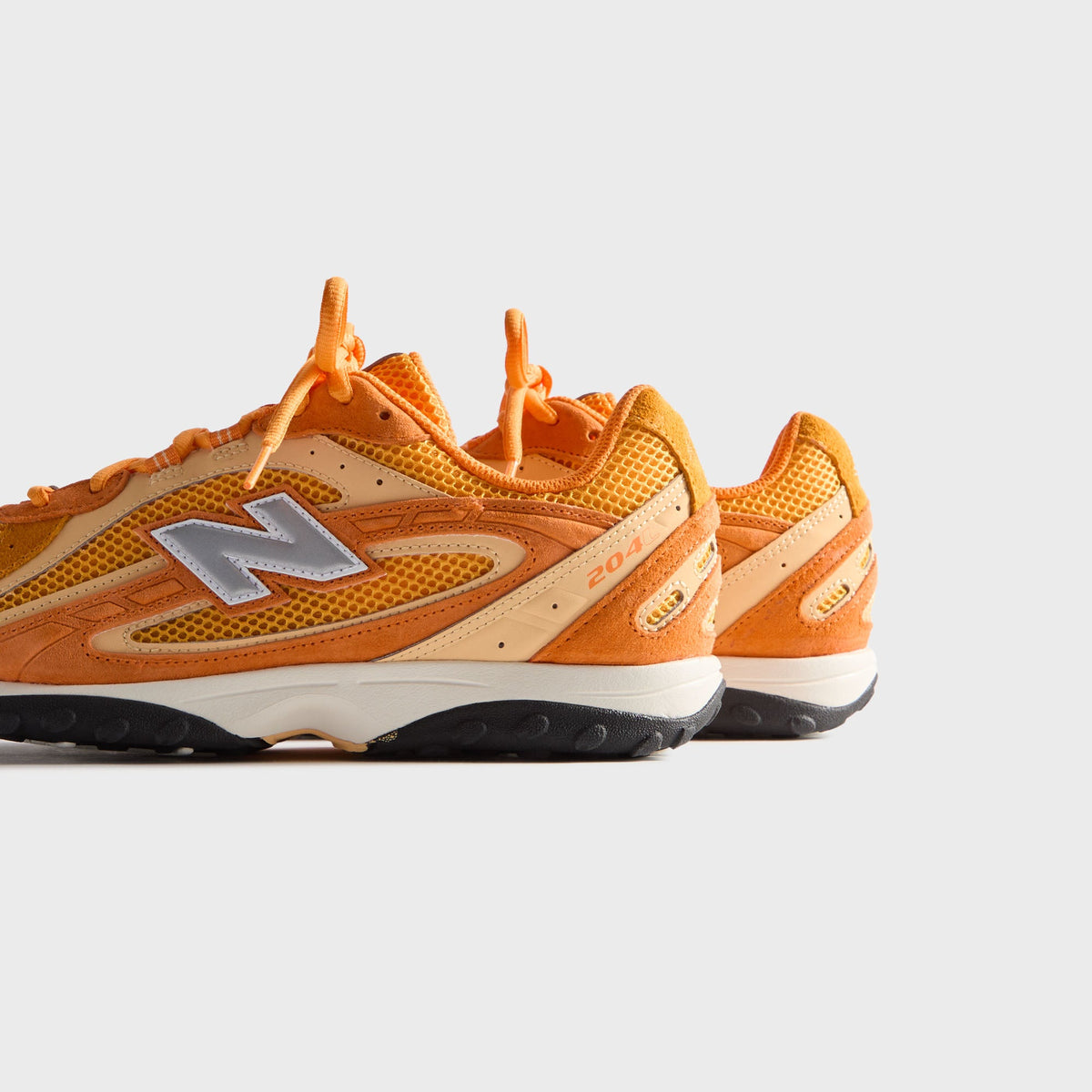 Kith & New Balance 204L in Sunburst, angled rear-side view of the pair showing 204 branding and orange suede heels