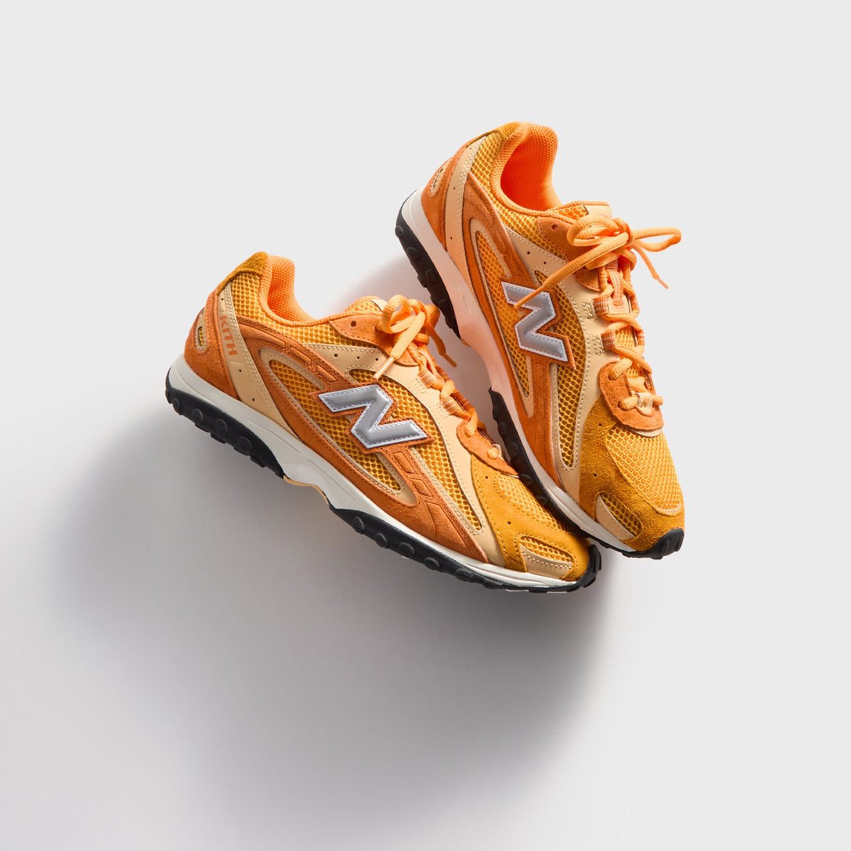 Kith & New Balance 204L in Sunburst, overhead angled view of the orange pair with laces and silver N logos up