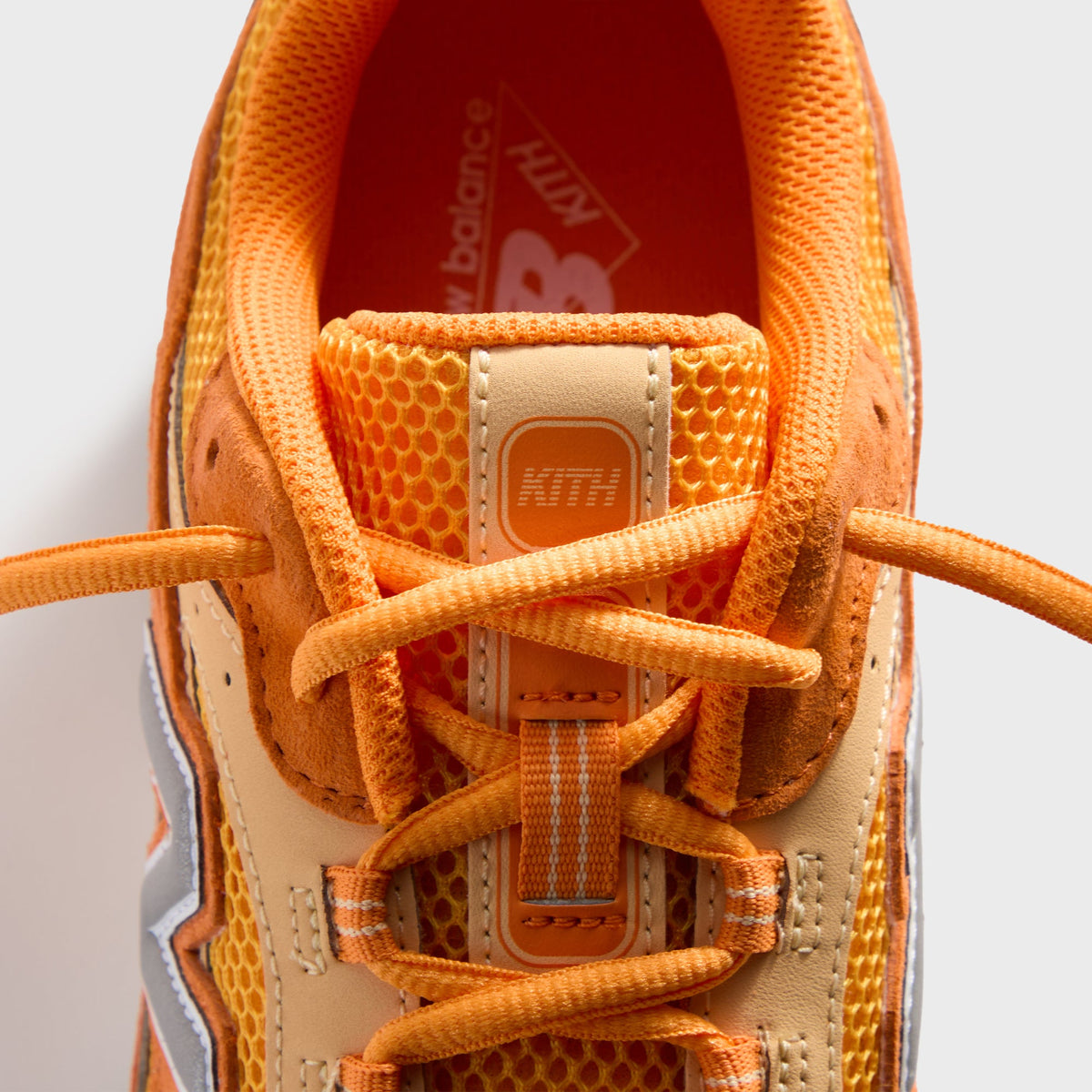 Kith & New Balance 204L in Sunburst, top-down close-up of the honeycomb-mesh tongue with KITH tab and orange laces