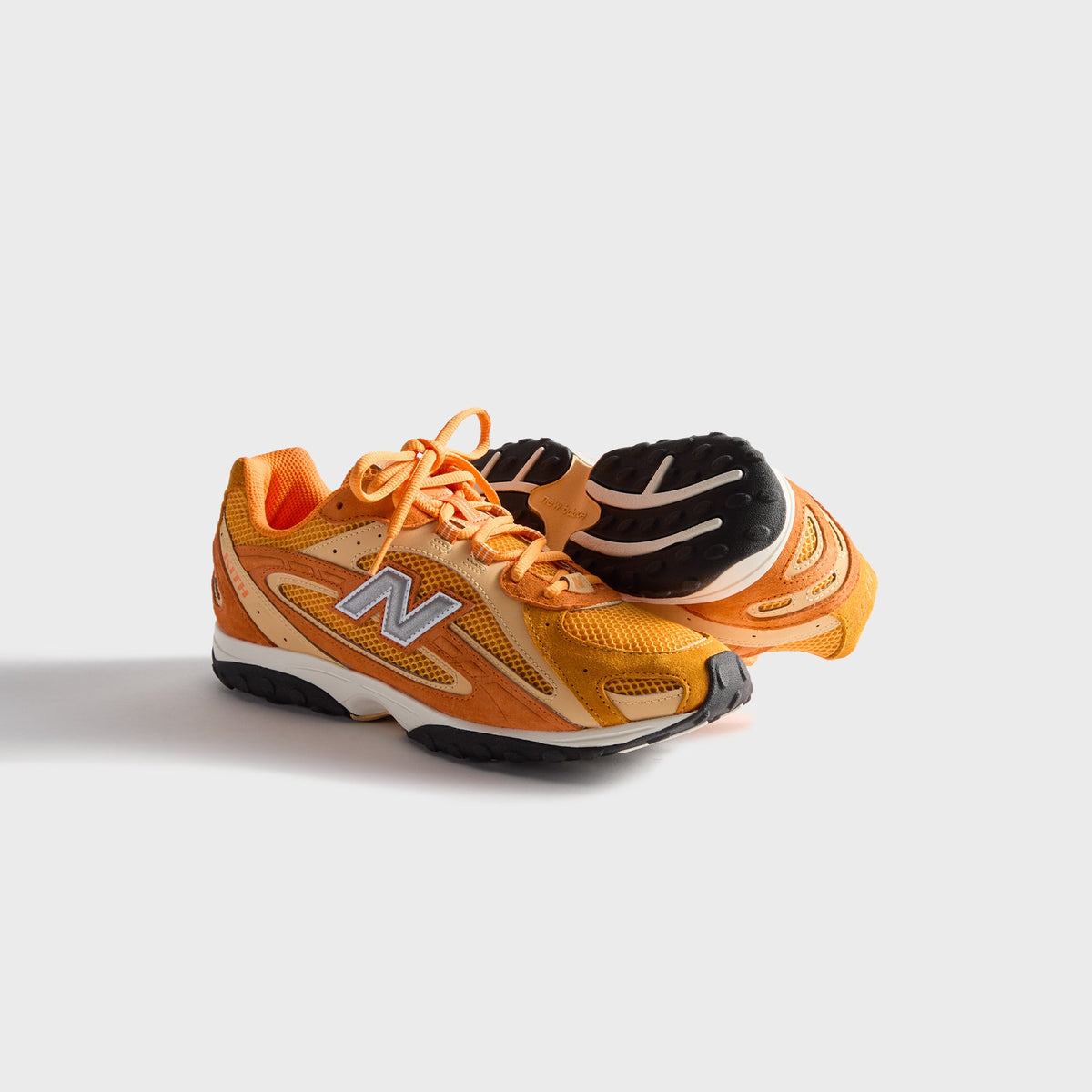 Kith & New Balance 204L in Sunburst, pair with one sneaker upright and one on its side showing the outsole
