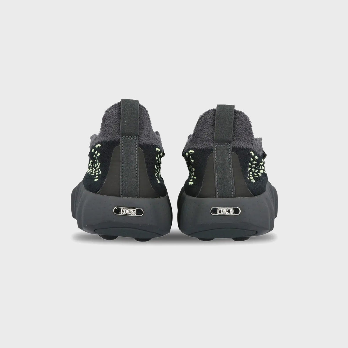 Rear view of Nike Mind 002 Flyknit in black and anthracite with metal heel plaque and nodular sole