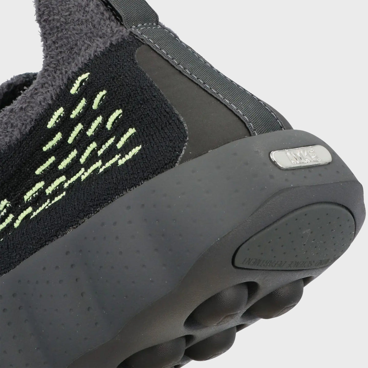 Close-up of Nike Mind 002 Flyknit heel with volt green stitching, metal Nike plaque and dark grey nodular sole