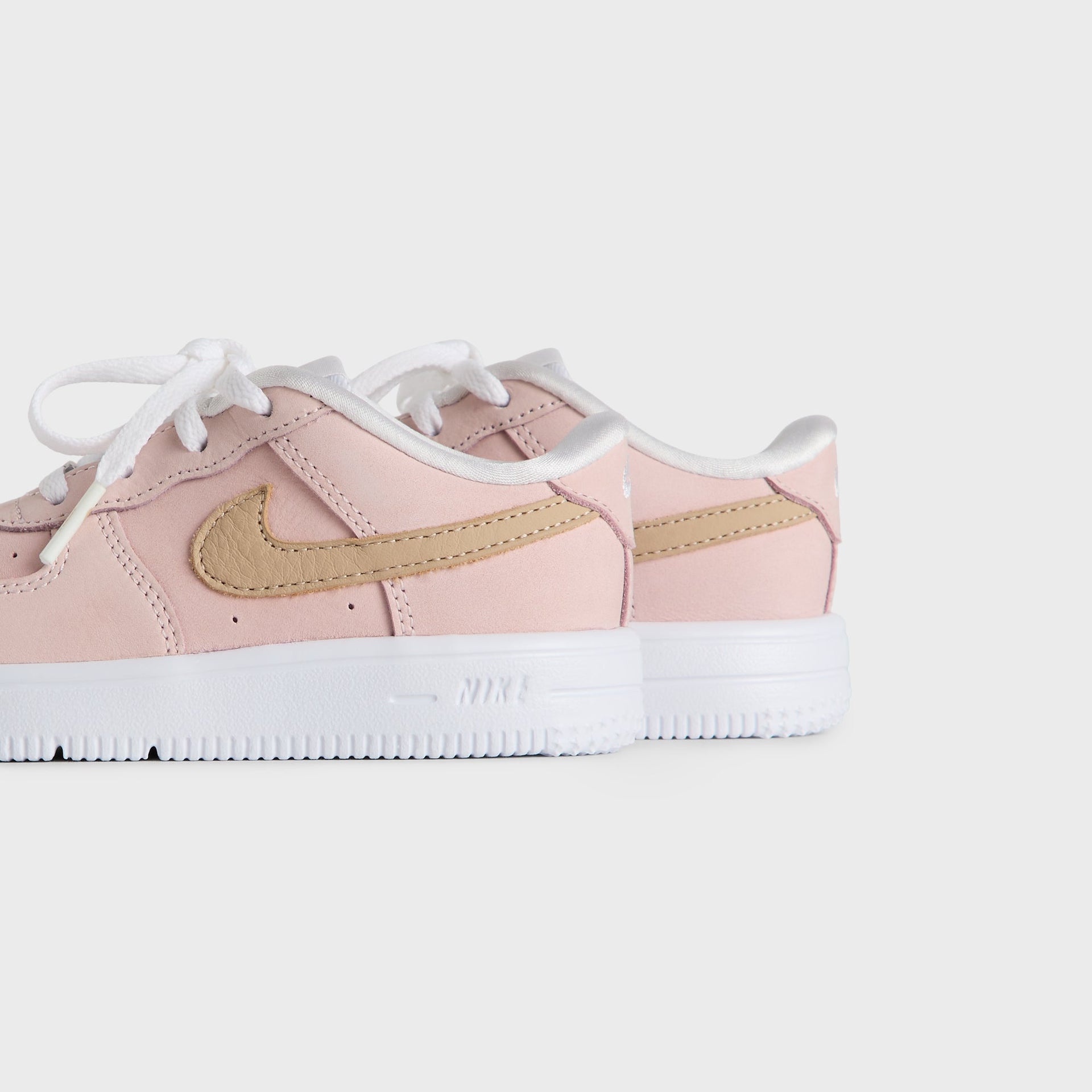 Kith Kids x Nike TD Air Force 1 Un-Linen pair viewed from the heel and outer side, pink leather on a white sole