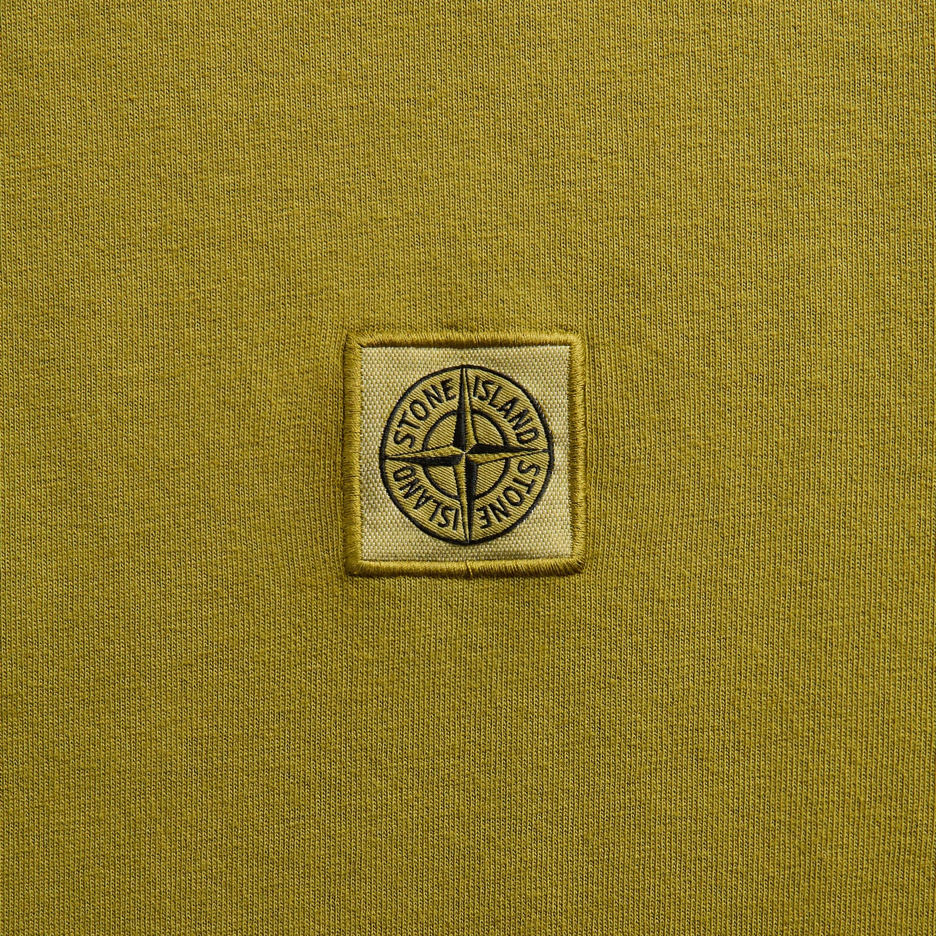 Close-up of Stone Island compass patch on cactus mustard-yellow tee chest