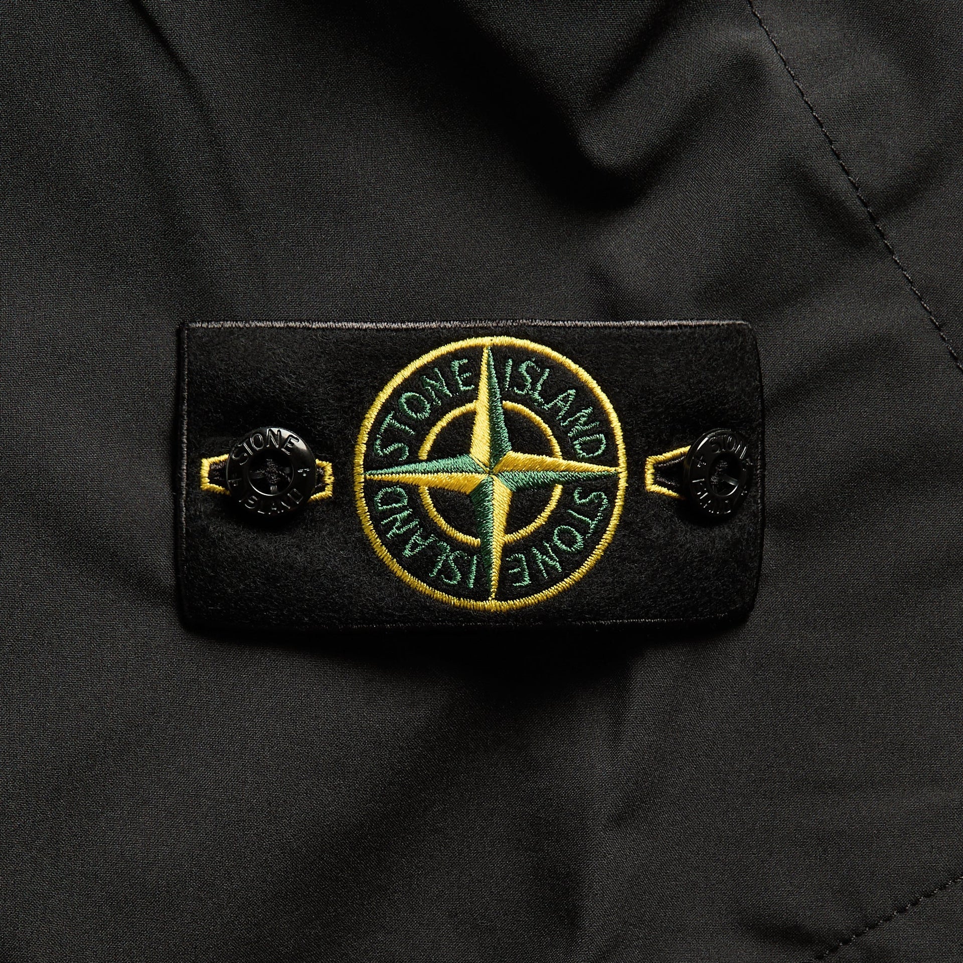 Close-up of black cargo trouser compass badge patch with buttoned tab