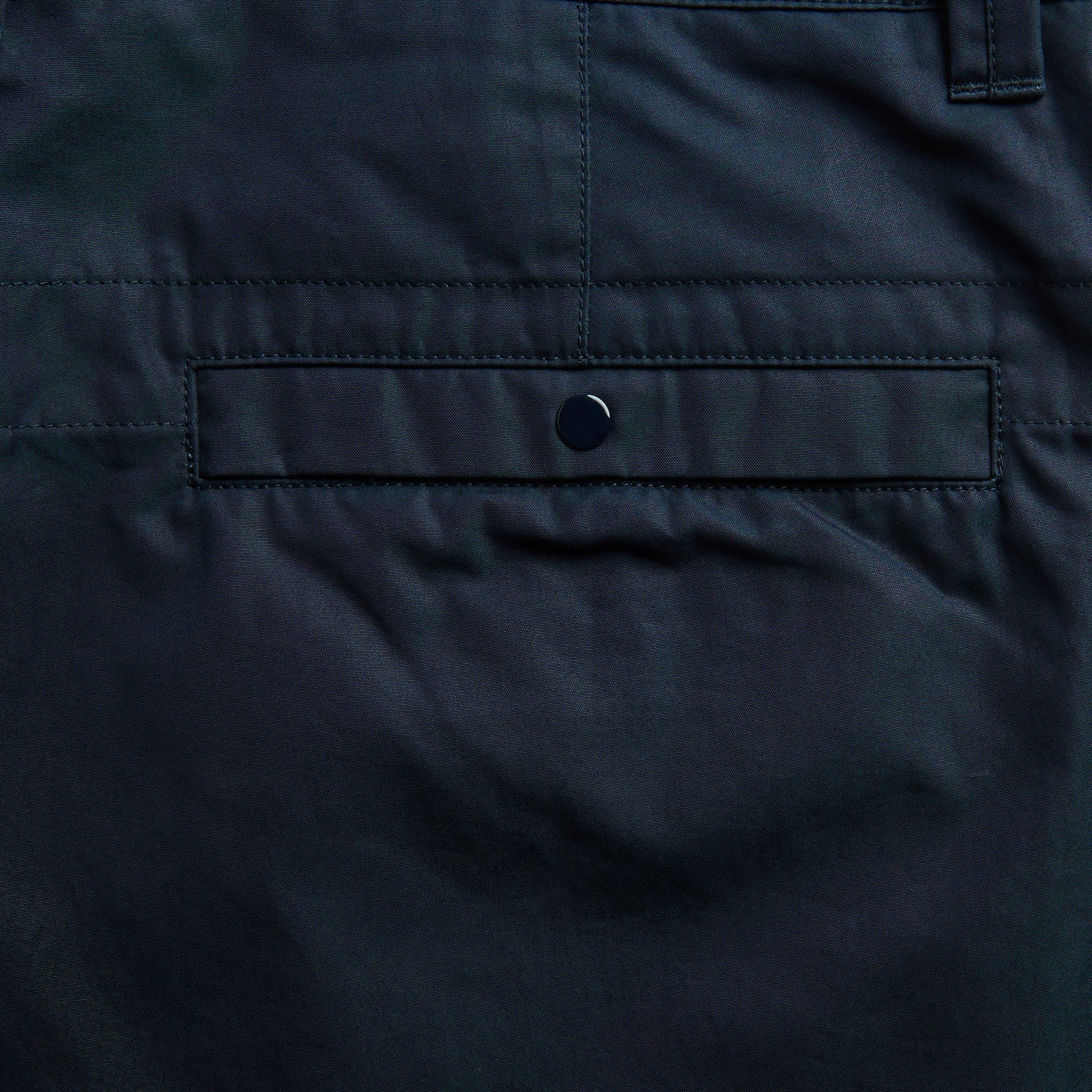 Close-up of navy chino trouser back welt pocket with snap-button closure