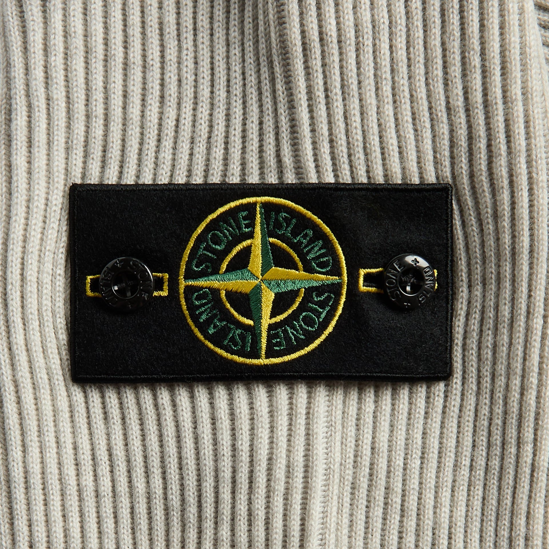 Stone Island sand melange ribbed wool crewneck, close-up of black compass-rose badge with buttons