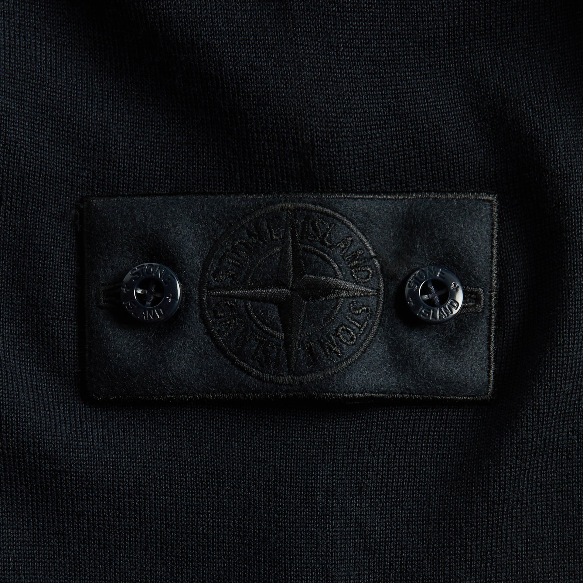 Close-up of tonal navy Stone Island compass badge and buttons on knit polo sleeve