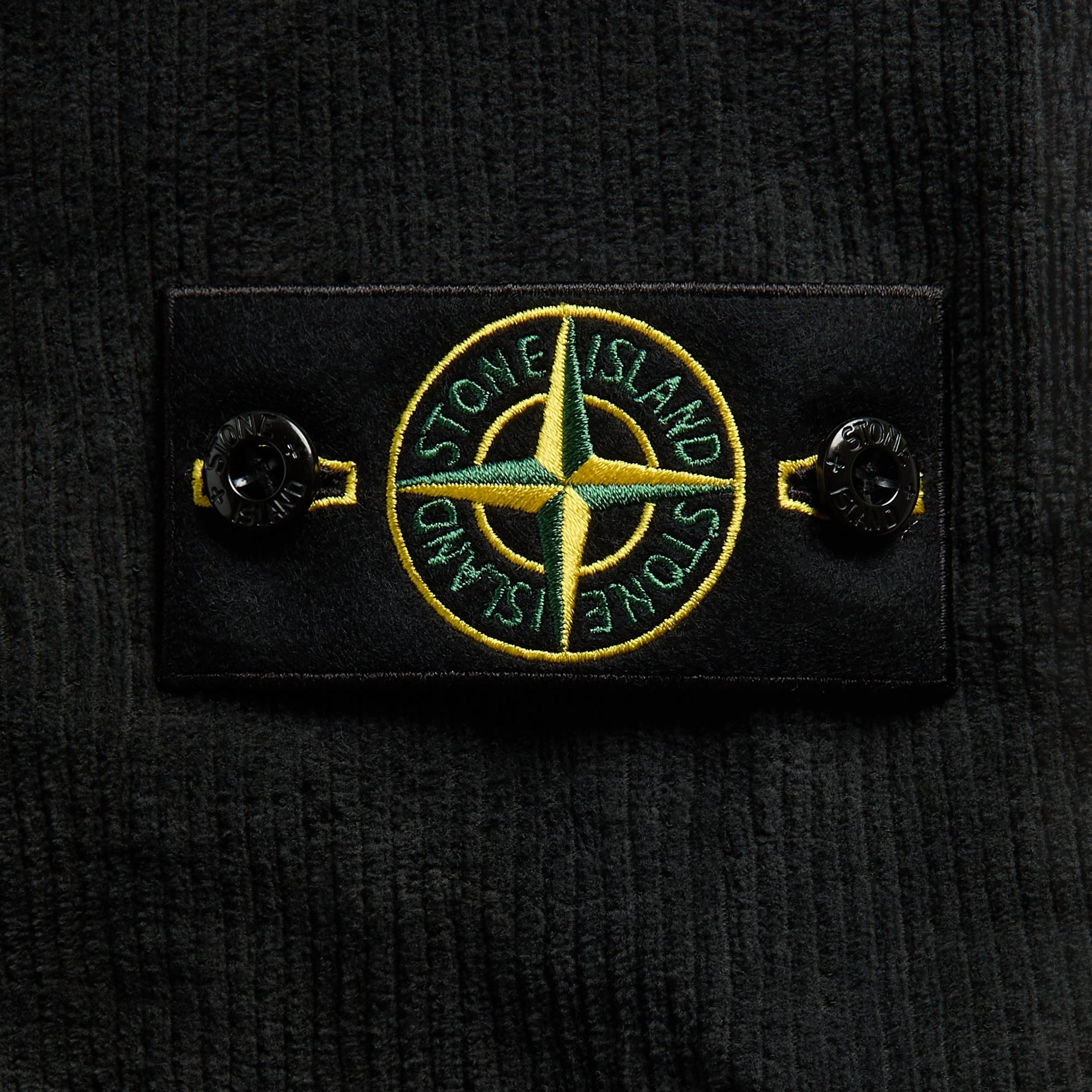 Close-up of Stone Island green and yellow compass badge on lead grey corduroy sleeve