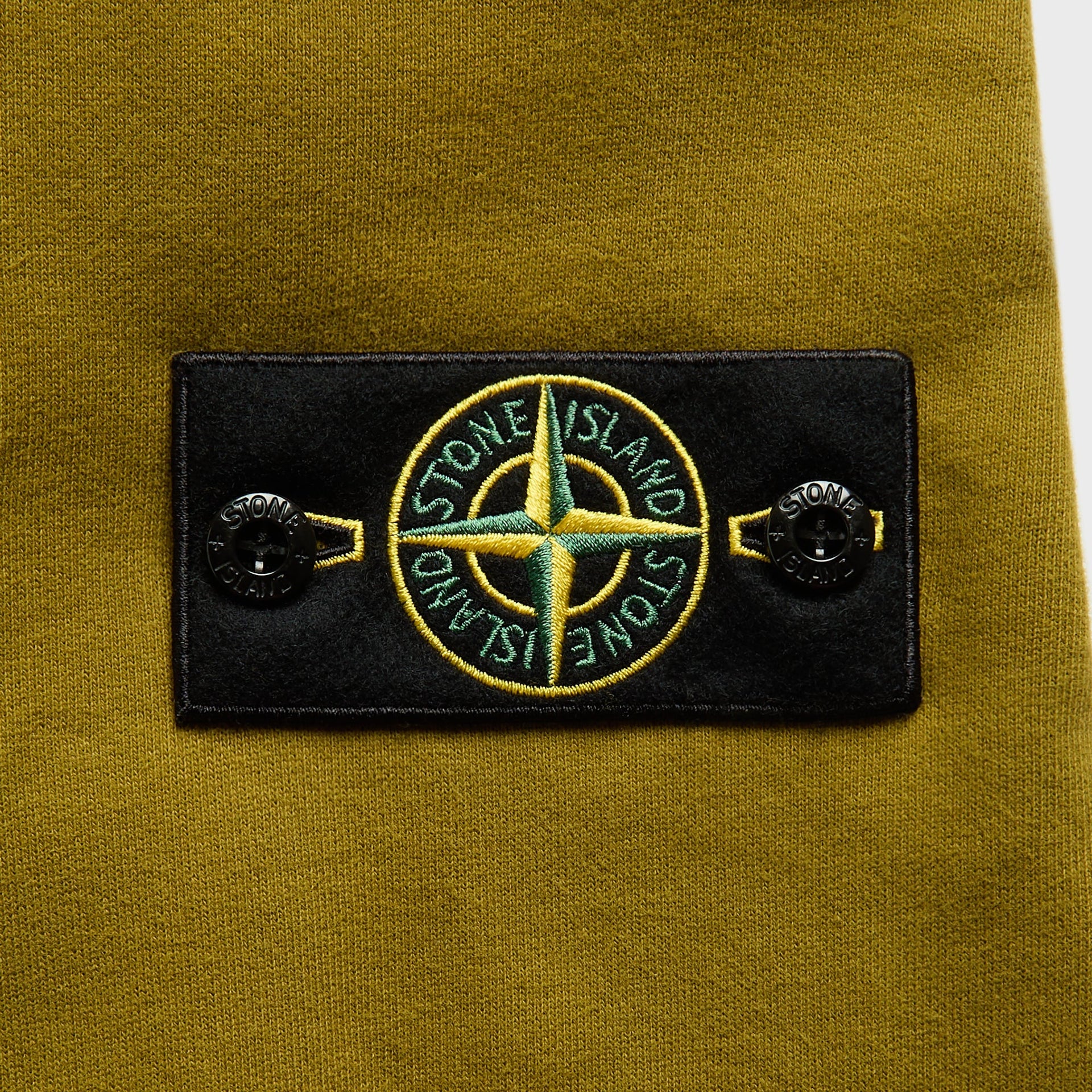 Stone Island cactus green fleece hoodie, close-up of black compass-rose badge with buttons on sleeve